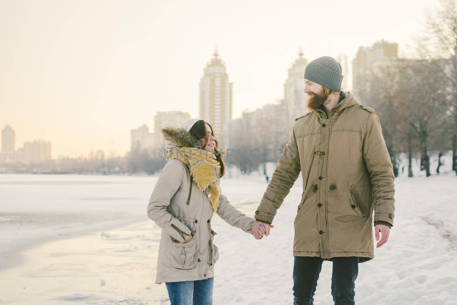Theme Christmas holidays winter new year. Young stylish Caucasian loving couple Heteresexual walking on the shore of a frozen lake. Date. Valentines Day in winter at sunset. Love and Romance Theme.