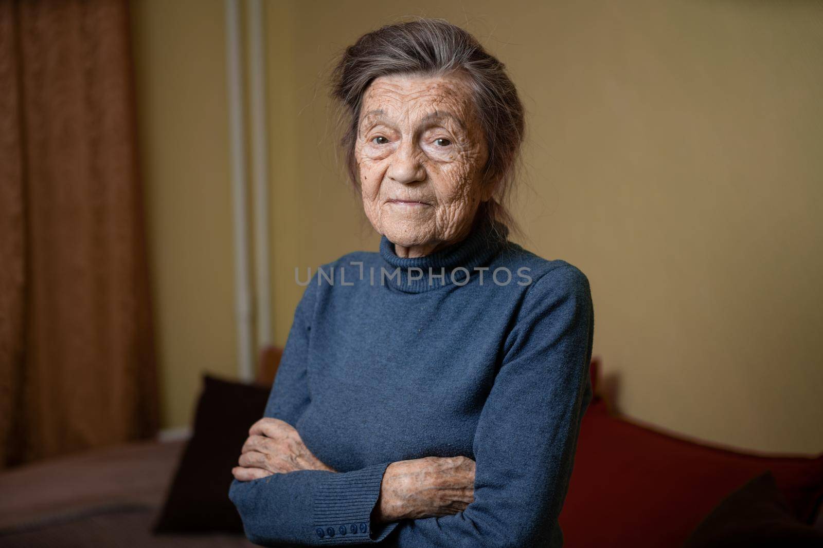 90 year old cute elderly woman with gray hair and wrinkles face, wearing sweater, portrait large, smiling and looking joyfully, background of room. Theme long-liver and aging, old people in good mood by Tomashevska