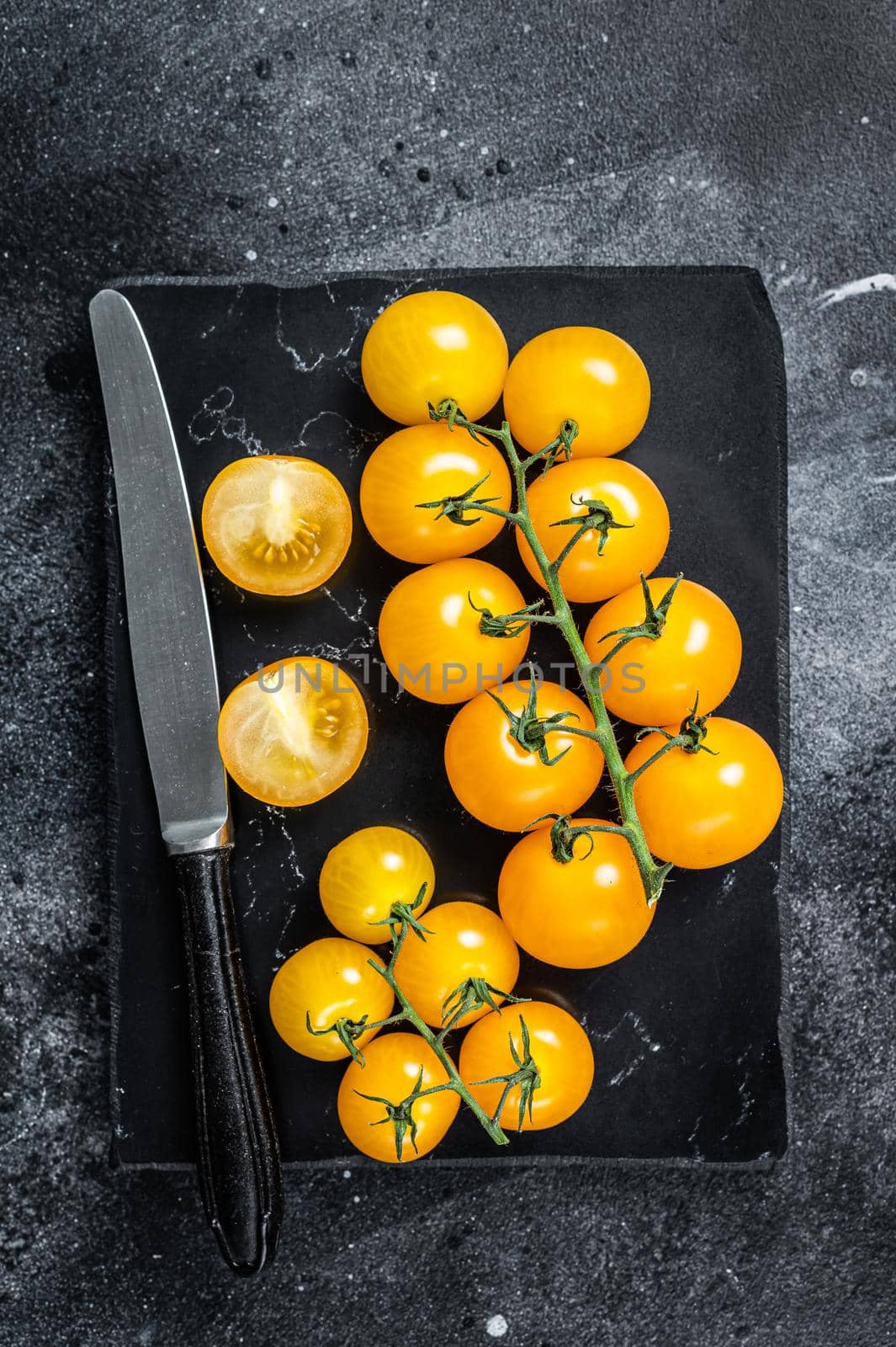 Bunch of yellow cherry tomato on a marble board. Black background. Top view.