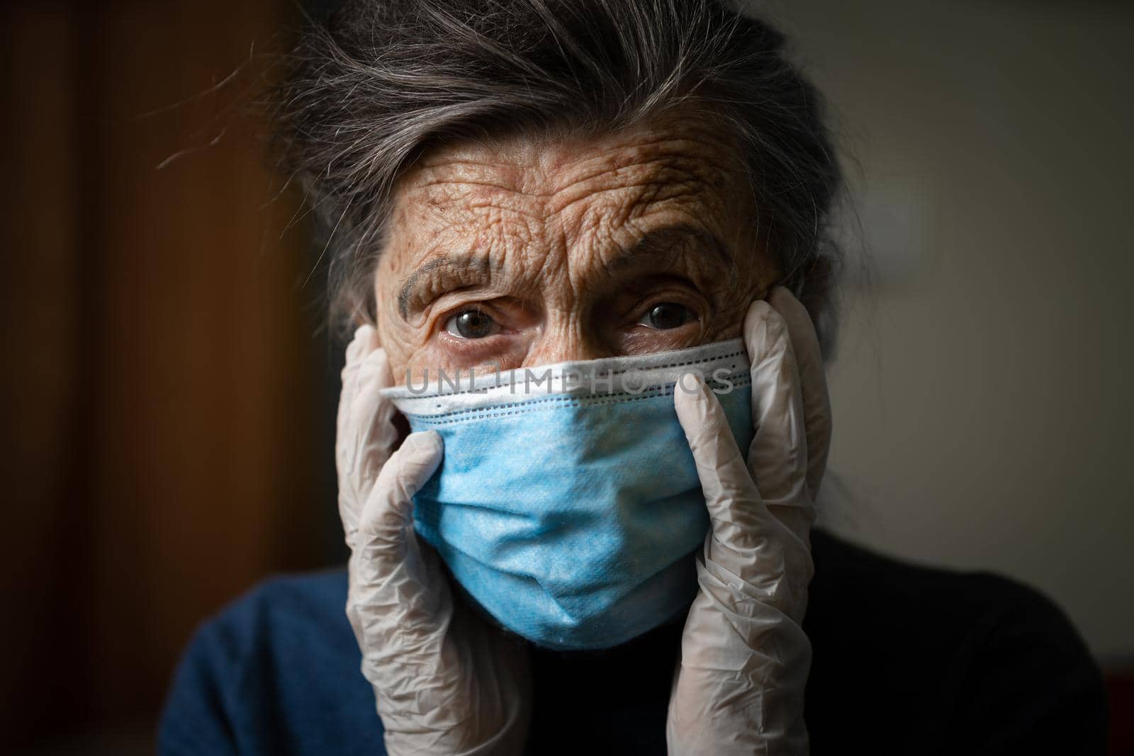 Portrait of an elderly Caucasian woman with wrinkles, wearing a medical mask and gloves, the emotion of fright and unpredictability due to the coronavirus epidemic. Elderly health and medicine theme by Tomashevska