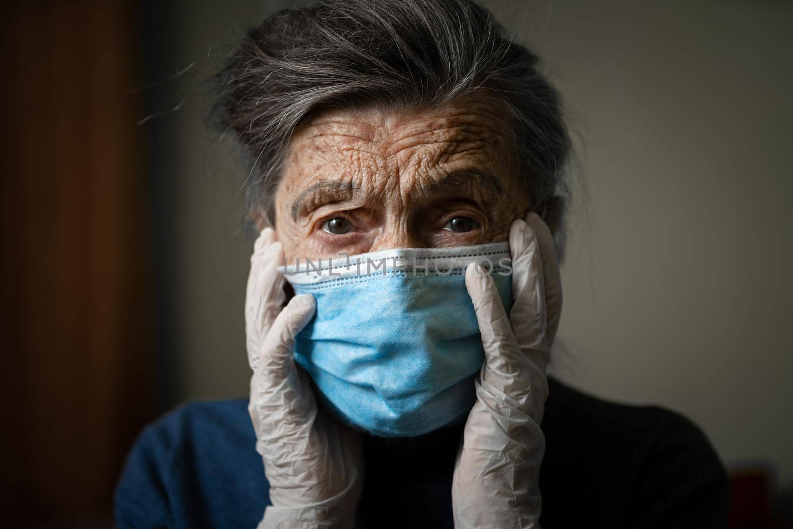 Portrait senior woman holding head hands, sad worried emotion in protective medical mask, gloves against virus and infection at home. Old gray hair female quarantine stay at home, loneliness and fear.