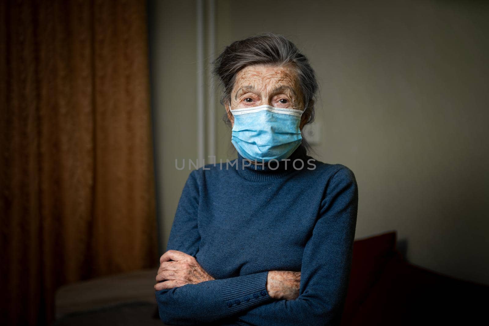 Senior woman in medical mask posing looking in camera at home. Topic help and support for old people during coronavirus epidemic. Elderly female is lonely during lockdown covid 19 in quarantine.