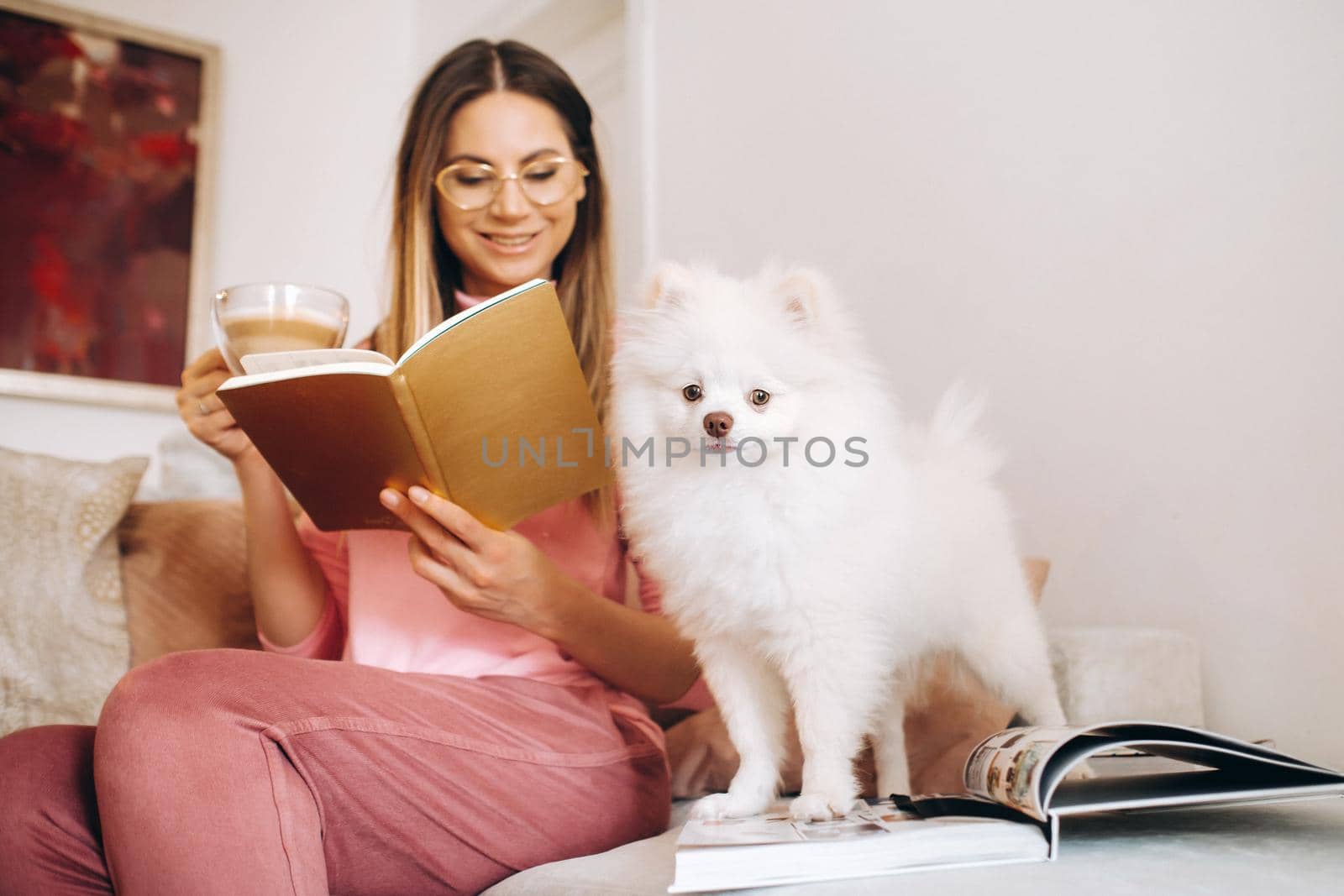 a girl in pajamas at home reads a book with her dog Spitzer, the Dog and its owner are resting on the sofa and reading a book.Household chores by Lobachad