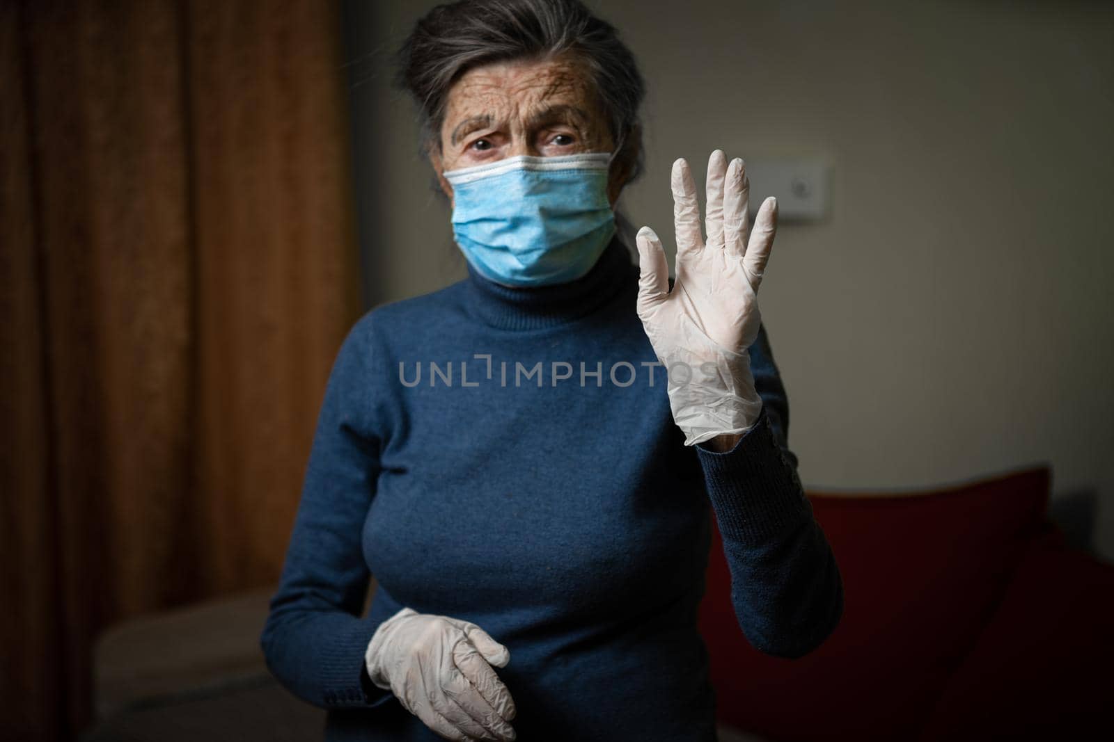 White medical glove in foreground, shown by an elderly grandmother wearing a medical mask, calling for safety and sanitation during an epidemic. Senior woman in personal protective equipment.