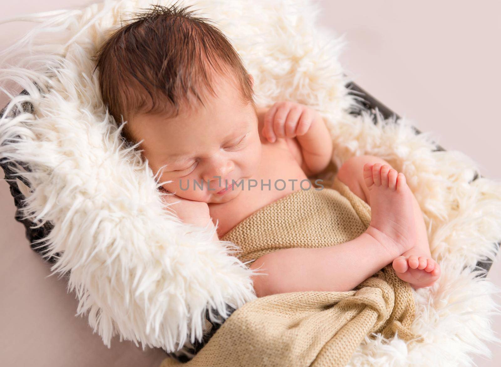 Little baby in light pink-red knitted beanie sweetly sleeping on the white coverlet in the basket on the light background