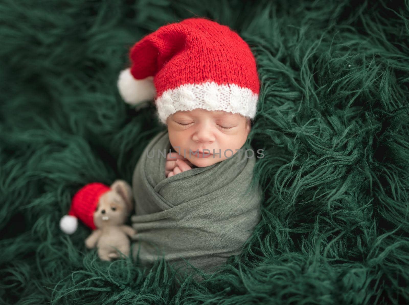 Adorable newborn in santa hat sleeping next to toy