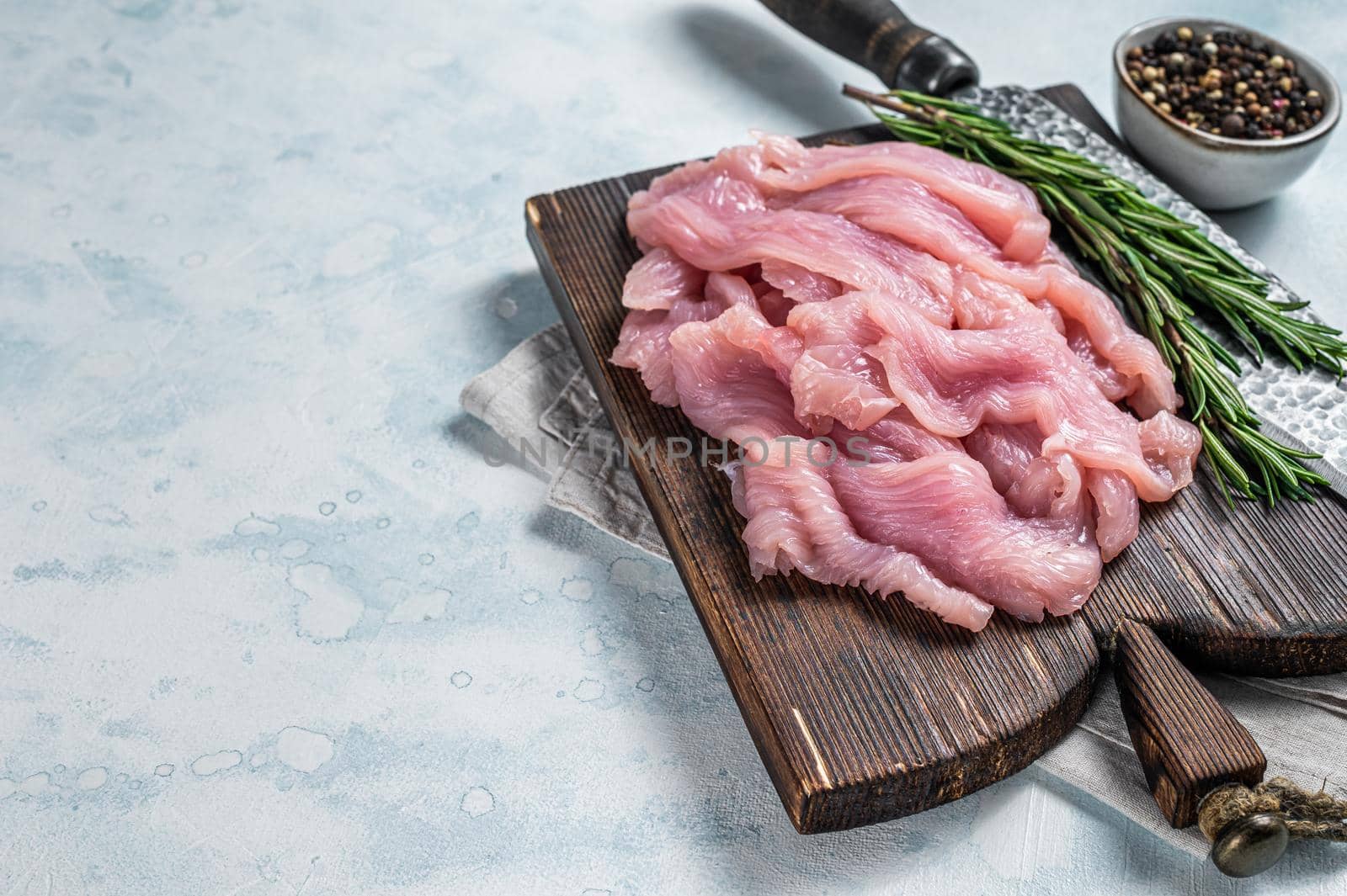 Sliced Raw turkey or chicken fillet meat on a cutting board with butcher knife. White background. Top View. Copy space by Composter