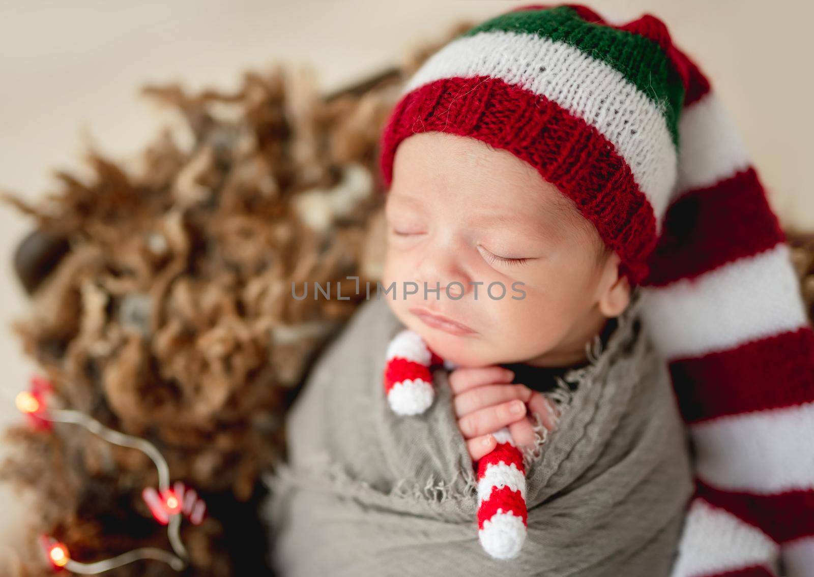 Funny newborn in christmas hat holding knitted candy