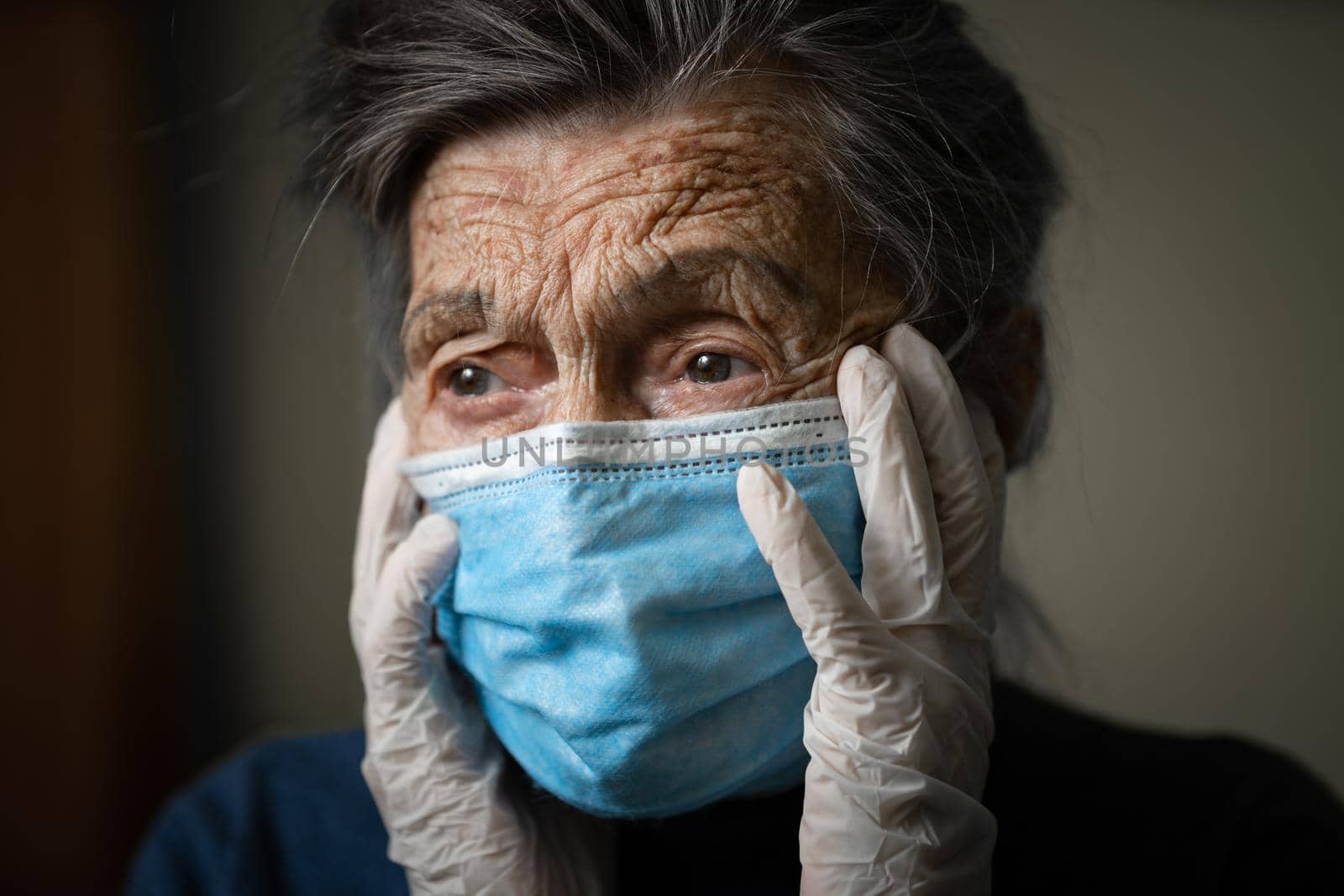 Portrait of an elderly Caucasian woman with wrinkles, wearing a medical mask and gloves, the emotion of fright and unpredictability due to the coronavirus epidemic. Elderly health and medicine theme.