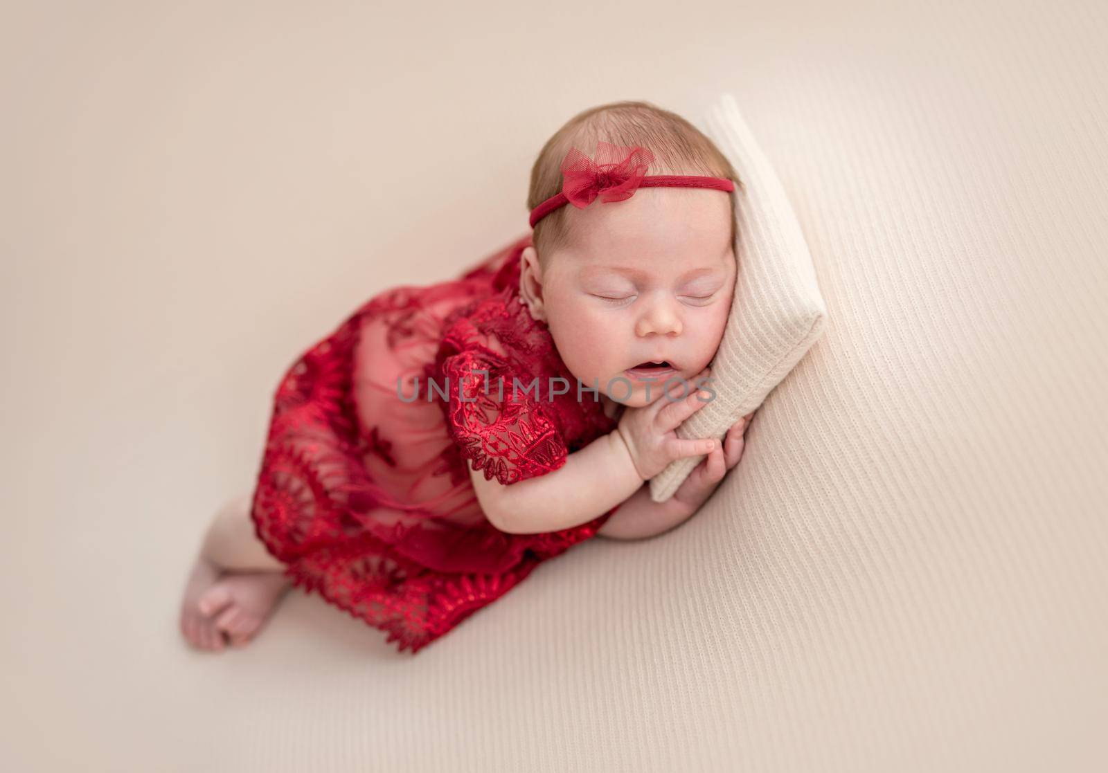 Cute newborn in red lace outfit resting on tiny pillow