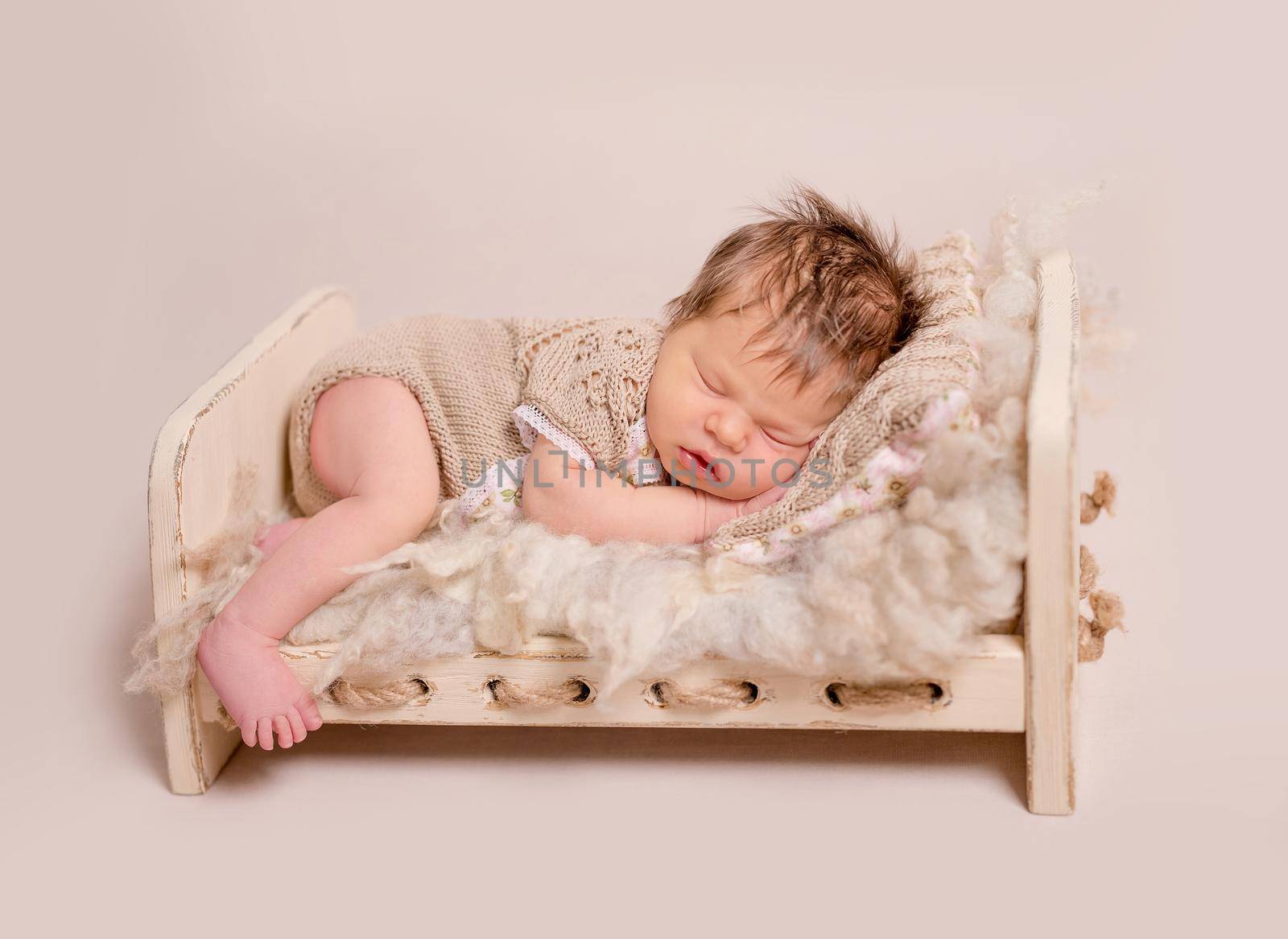 Cute little baby in knitted brown suit sweetly sleeping on the woolen blanket in little bed