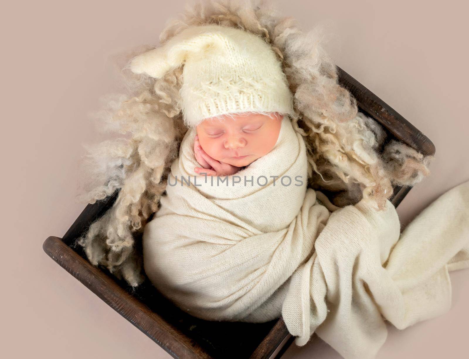 Cute little baby in hat sweetly sleeping in small bed covered in blanket