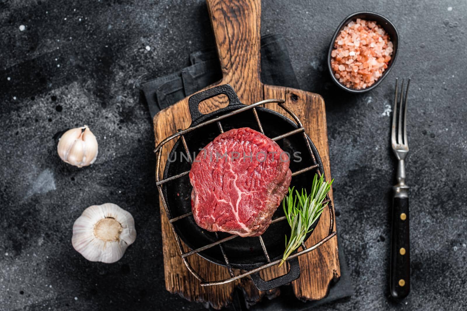 Raw fillet mignon beef steak on a grill with herbs. Black background. Top view.