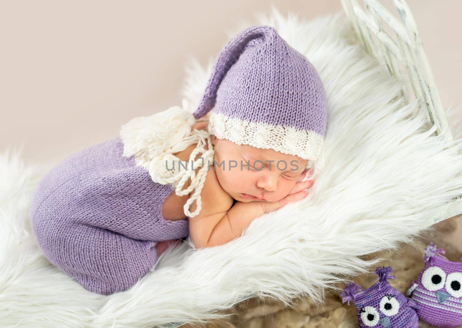 Cute little baby in white and purple knitted suit sweetly sleeping in small bed