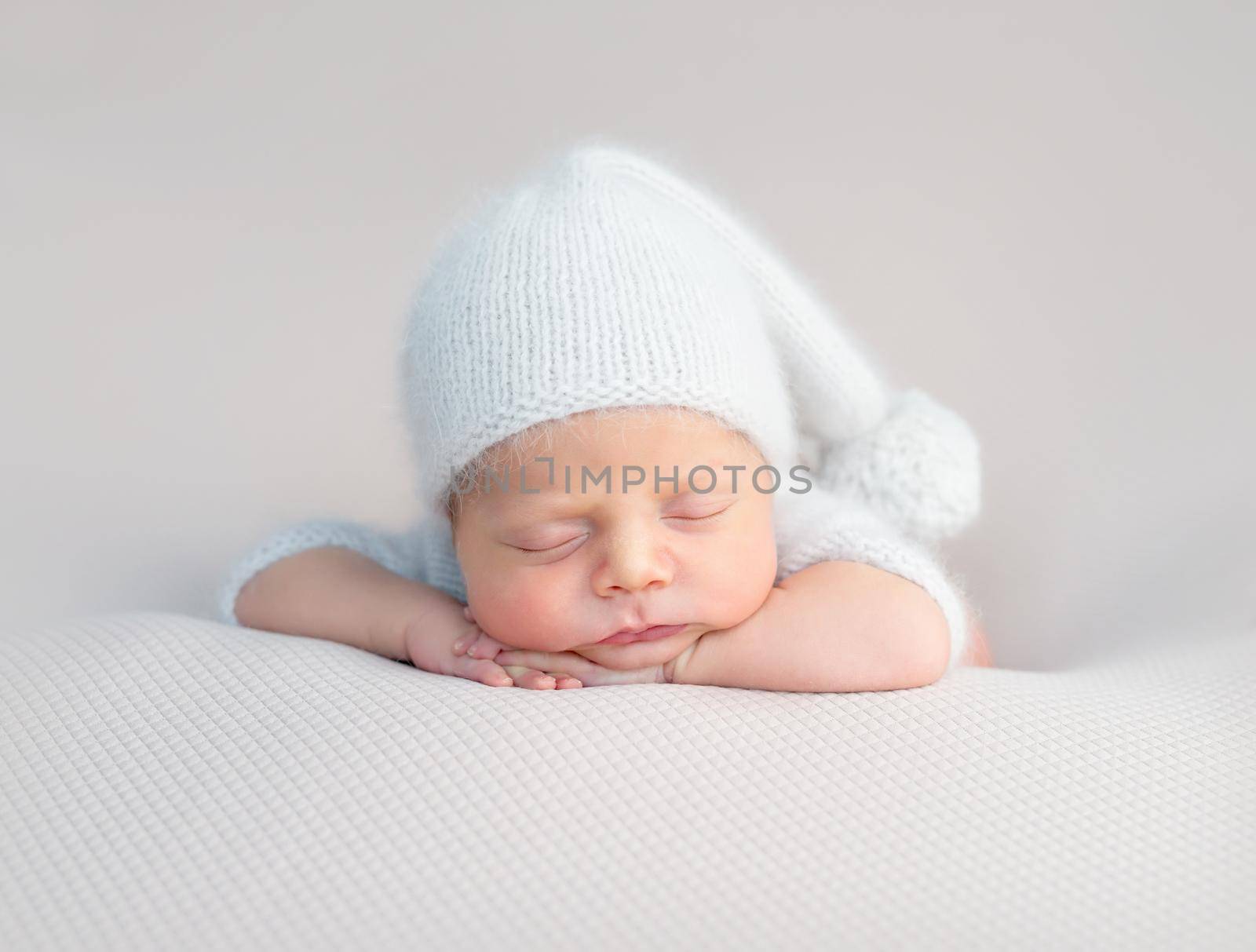 Cute little baby in white hat and knitted suit sweetly sleeping