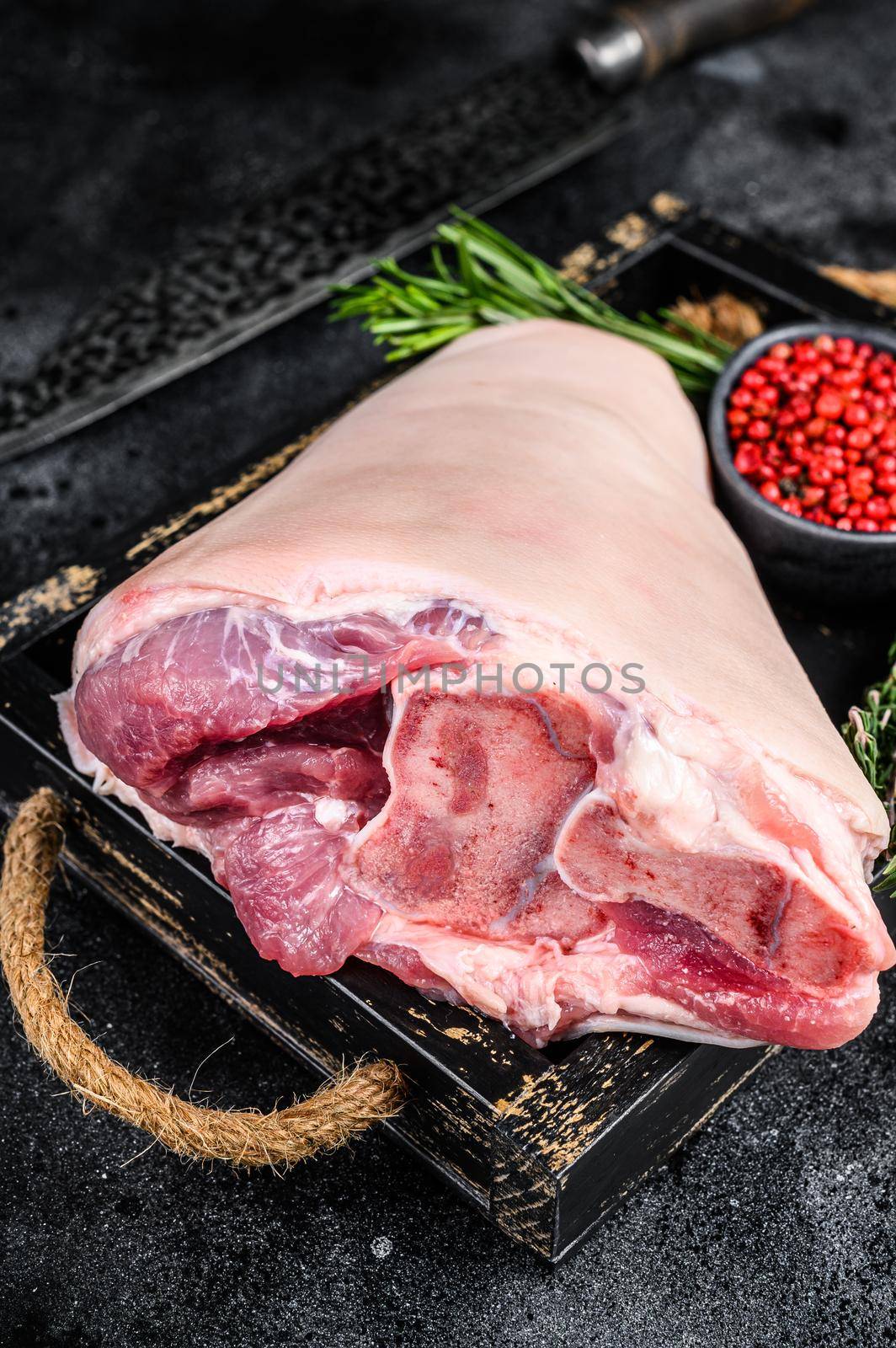 Fresh Raw pork Eisbein knuckle ham in a wooden tray with meat knife. Black Wooden background. Top view by Composter