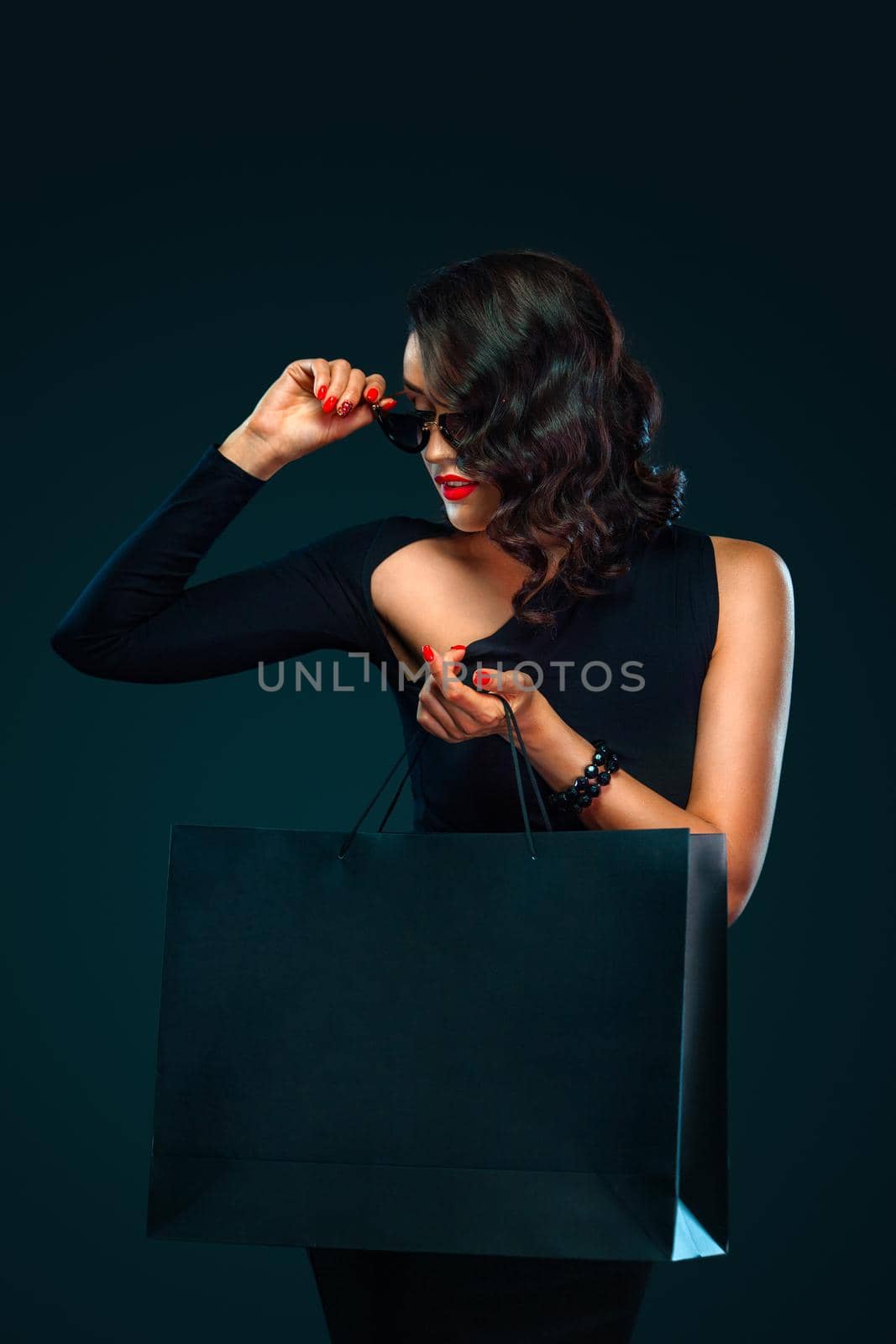 Black Friday sale concept for shop. Beautiful girl in sunglasses holding big bag isolated on dark background at shopping on blackfriday. by MikeOrlov