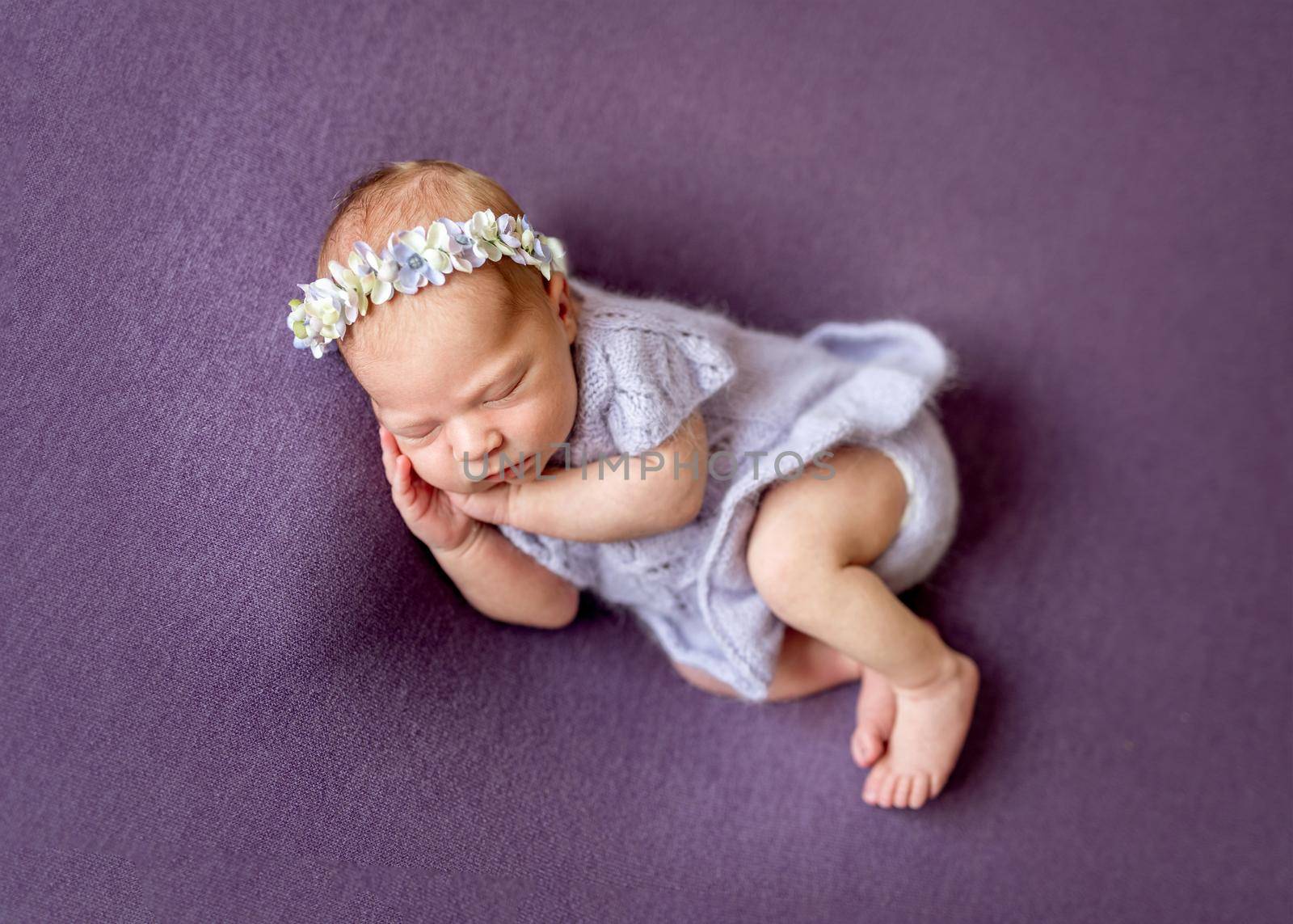 Quiet newborn in cute knitted violet blue wool jacket and floral headband