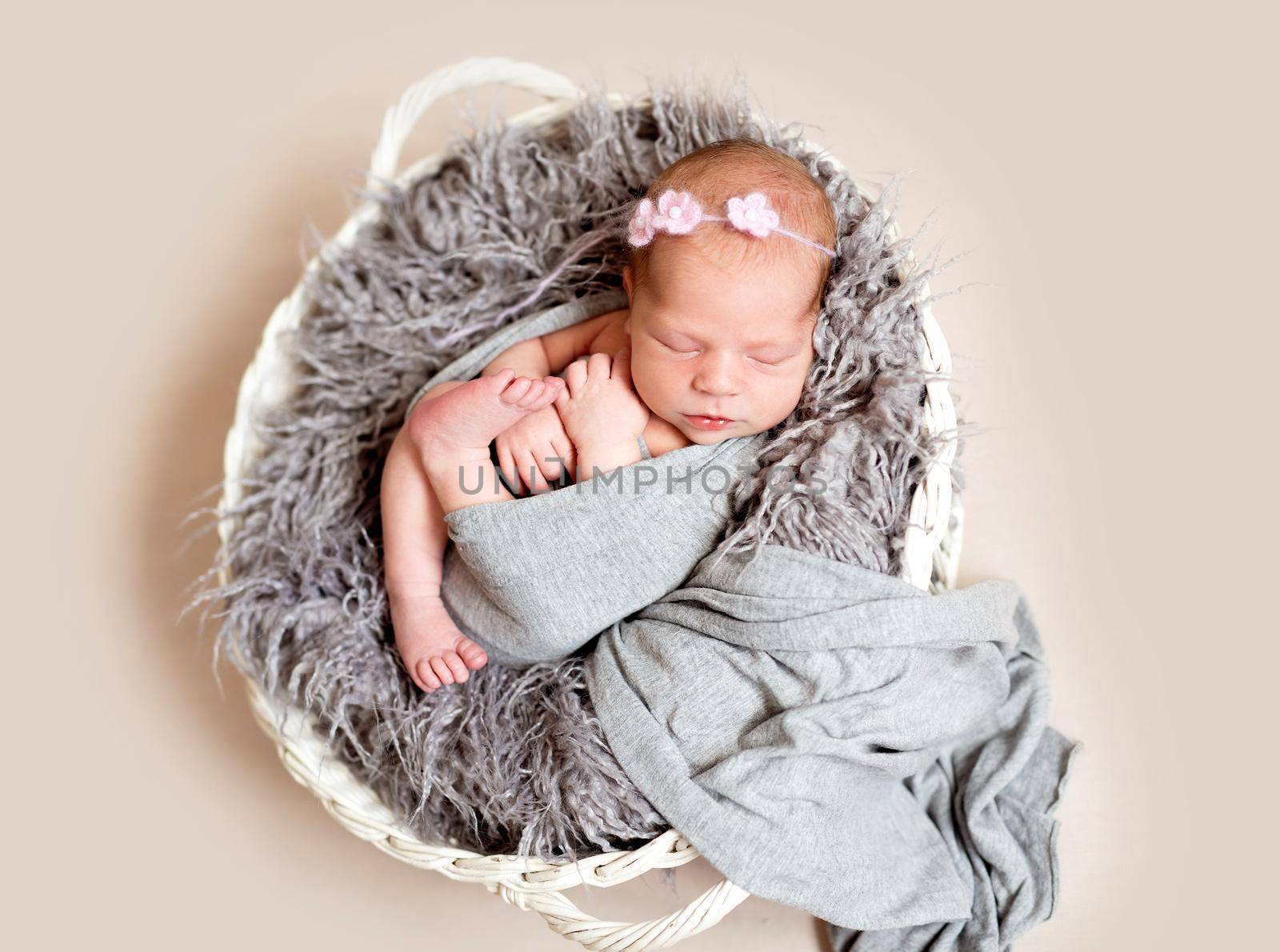 Newborn baby in grey blanket with floral headband sleeping in basket