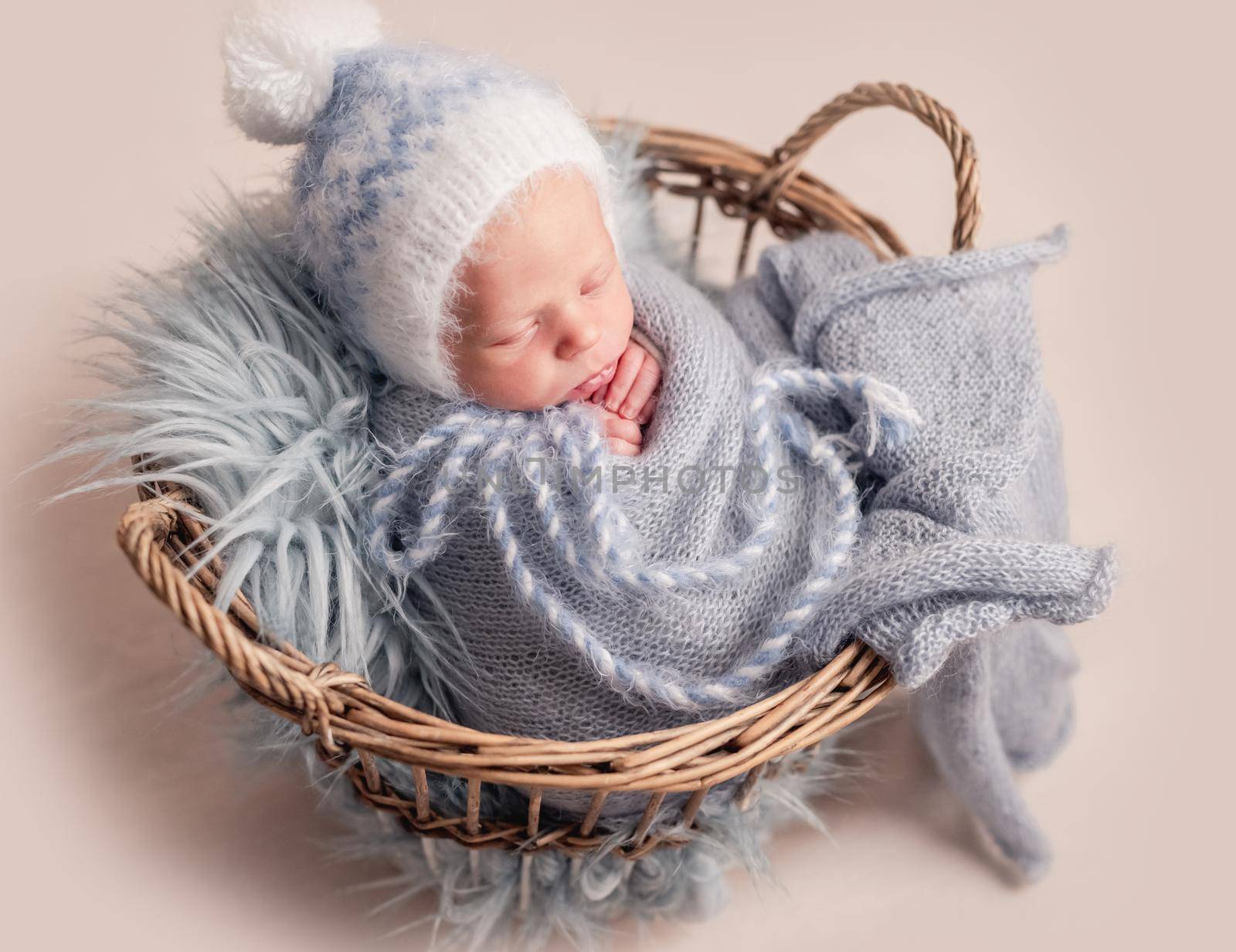 Top view of baby in big hat sleeping in basket covered in blue blanket
