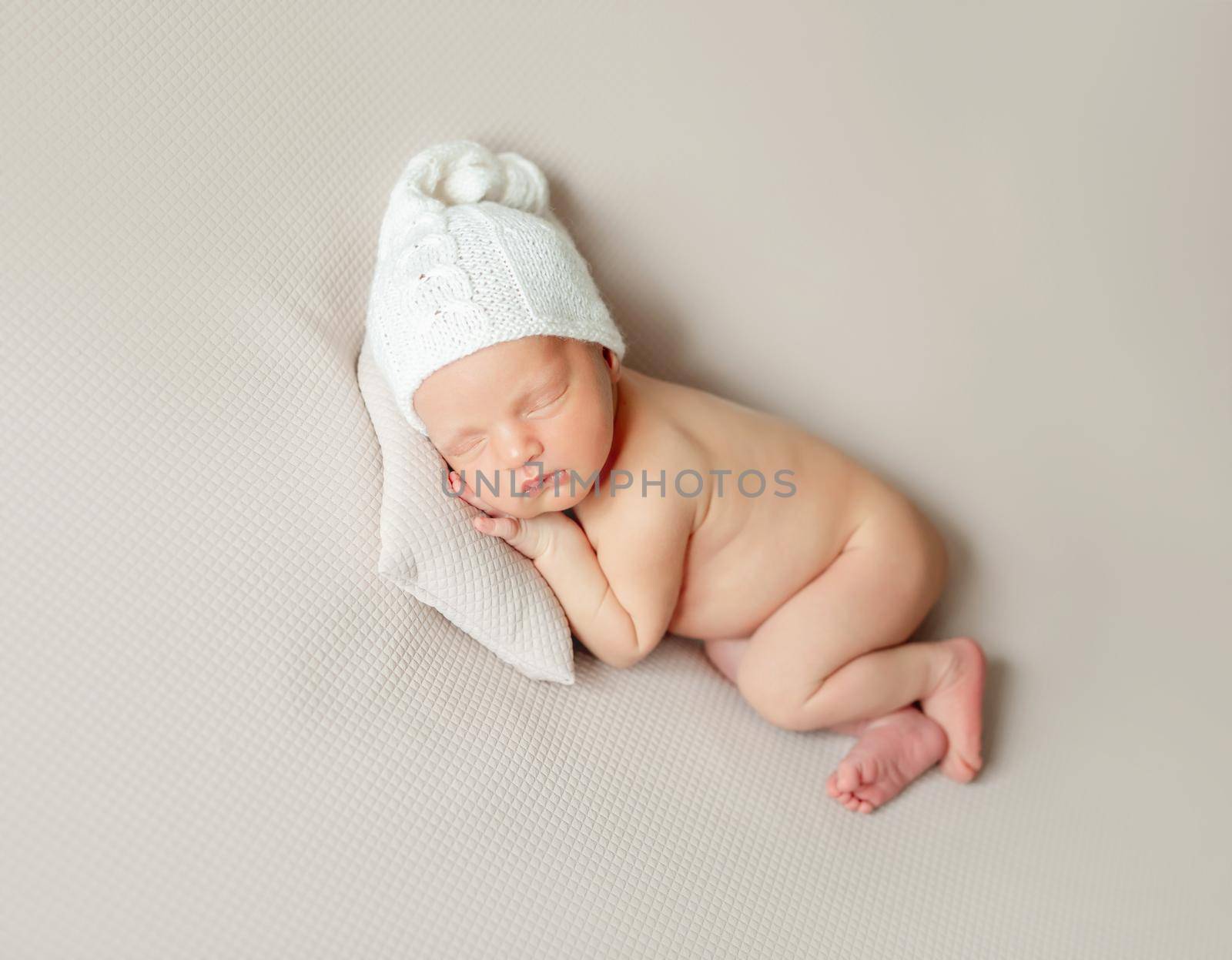 Adorable little baby in knitted hat sleeping on small pillow on cream background