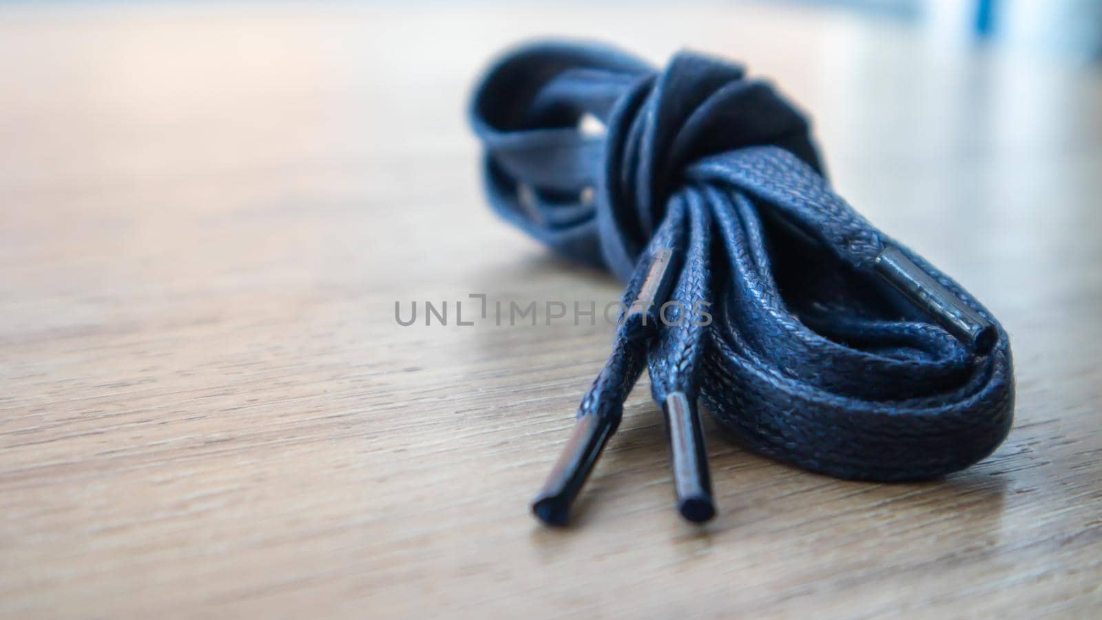 A subject shot of dark blue flat laces with thin tips for shoes rolled up and isolated on a wooden background. Stylish accessory