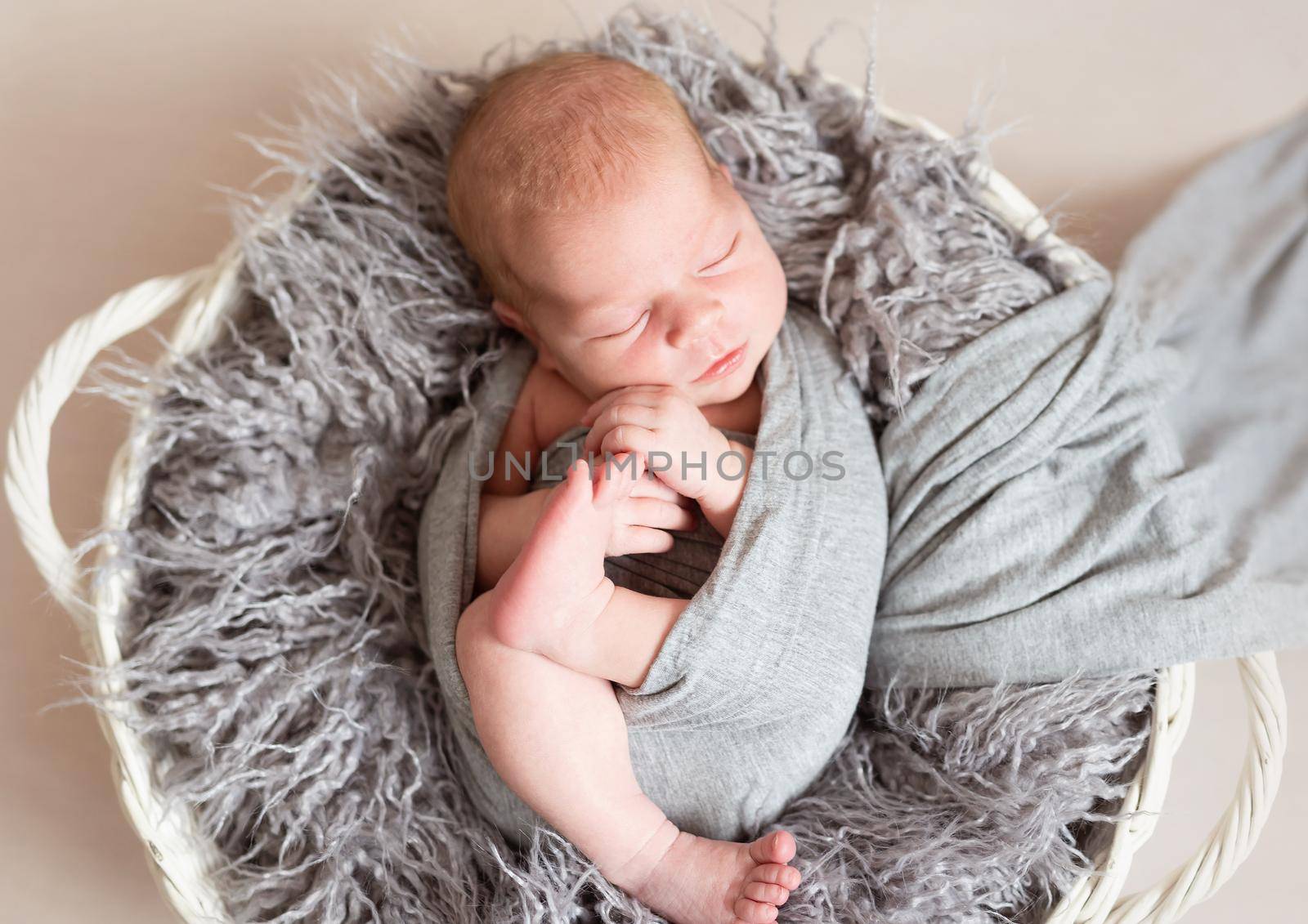 Newborn baby in grey blanket with floral headband sleeping in basket