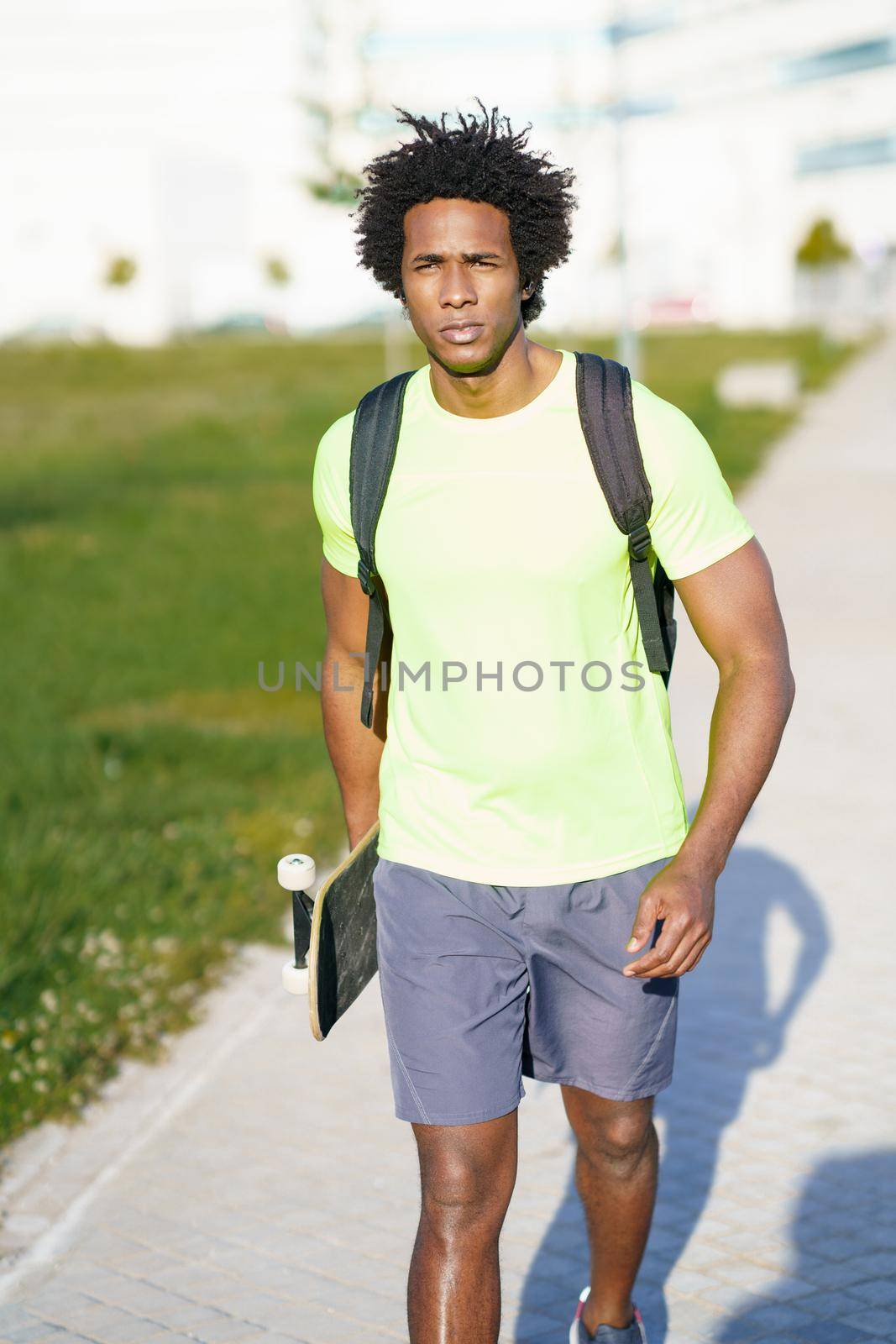 Black man with afro hair, going for a workout in sportswear and a skateboard.