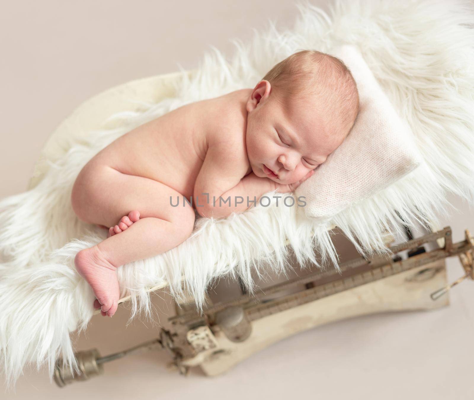 Cute newborn baby on a retro weight scale, isolated on beige background