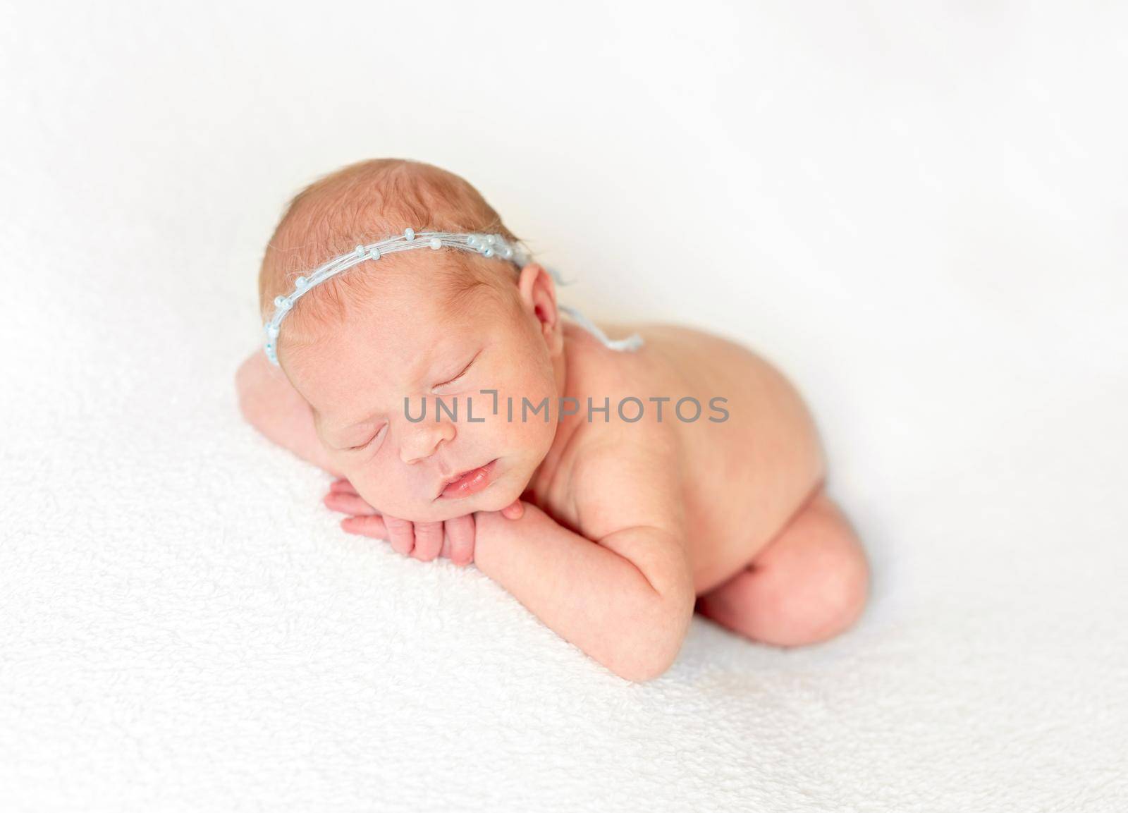 Naked innocent baby laying on fabric bedcover with headband