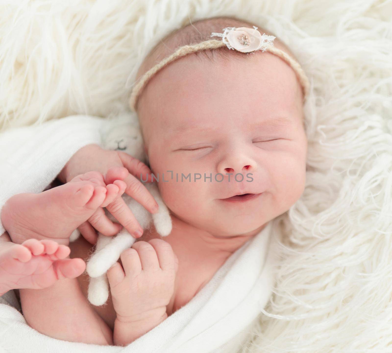 smiling newborn baby girl sleeping sweetly with a small toy