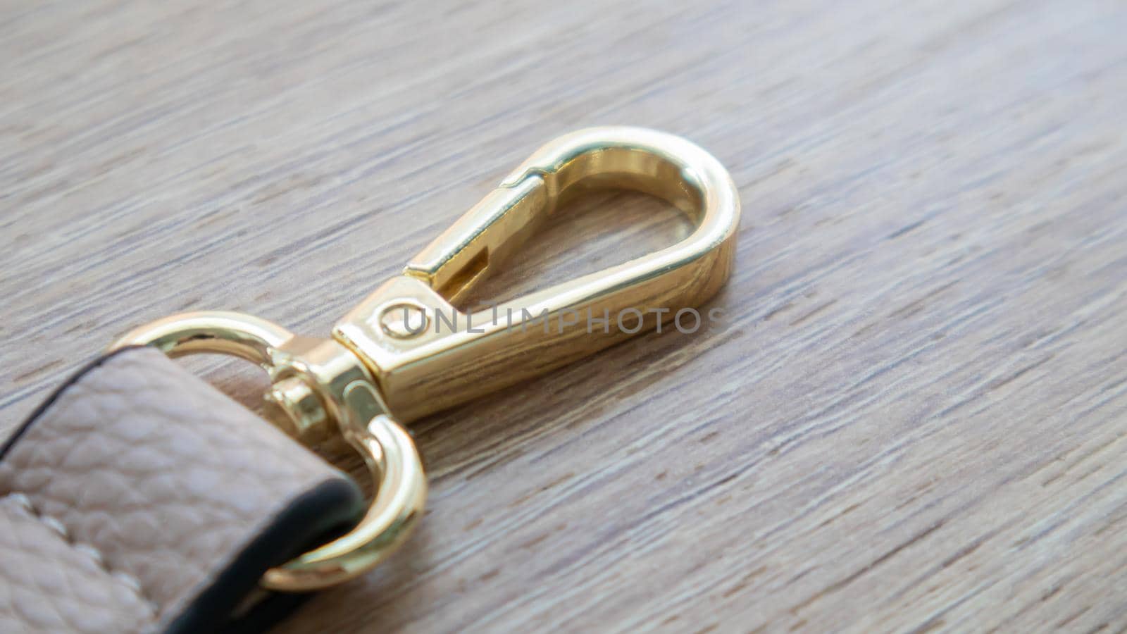 Swivel snap fastener with leather beige bag strap on a wooden background. Metal carabiner with swivel clip or hook. Small gold fittings close-up in selective focus