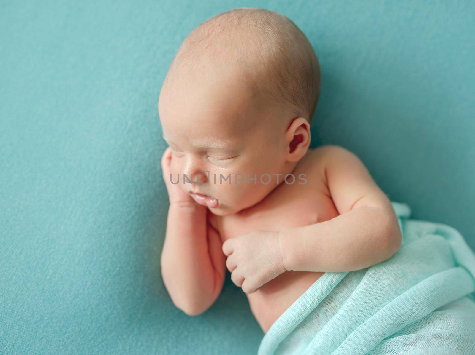 Little newborn wrapped in blue blanket resting in room