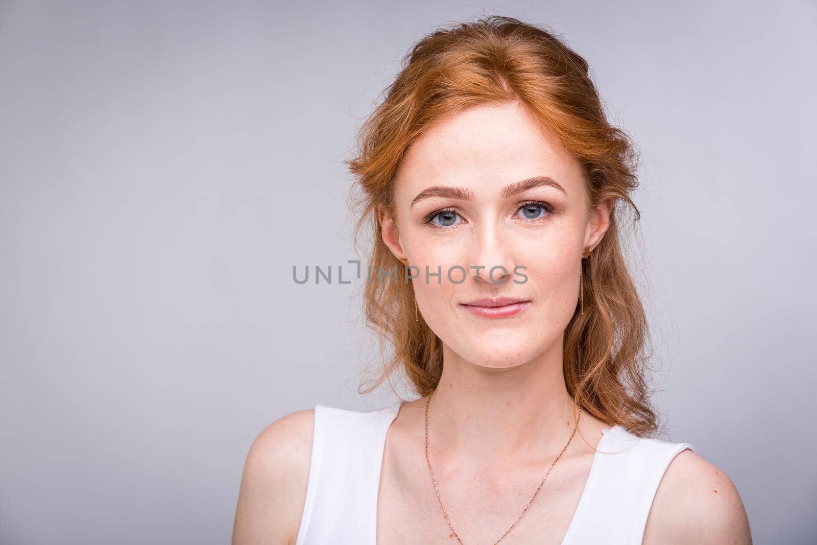 Portrait of a beautiful young woman of European, Caucasian nationality with long red hair and freckles on her face posing on a white background in the studio. Close-up student girl in a white blouse.
