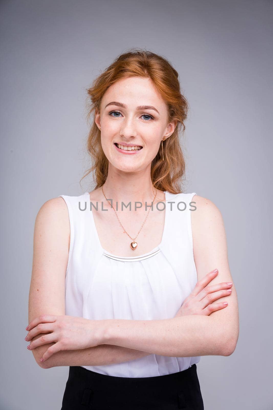 portrait vertical up to the waist young, beautiful business woman, student with lred, curly hair and freckles on gray background. SHe dressed in a white blouse with short sleeves about open shoulders.