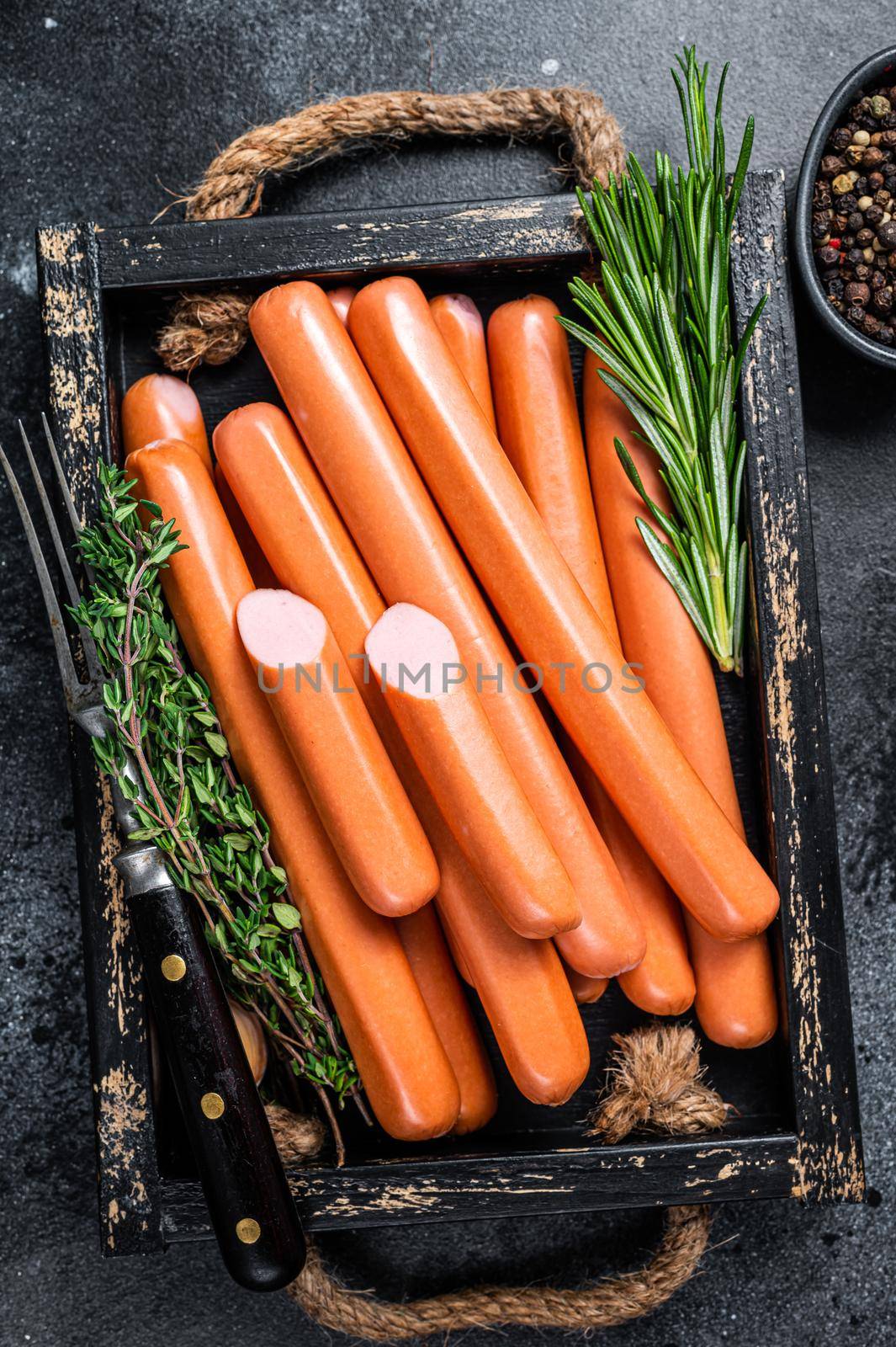 Frankfurter sausages in a wooden tray with herbs. Black background. Top view by Composter