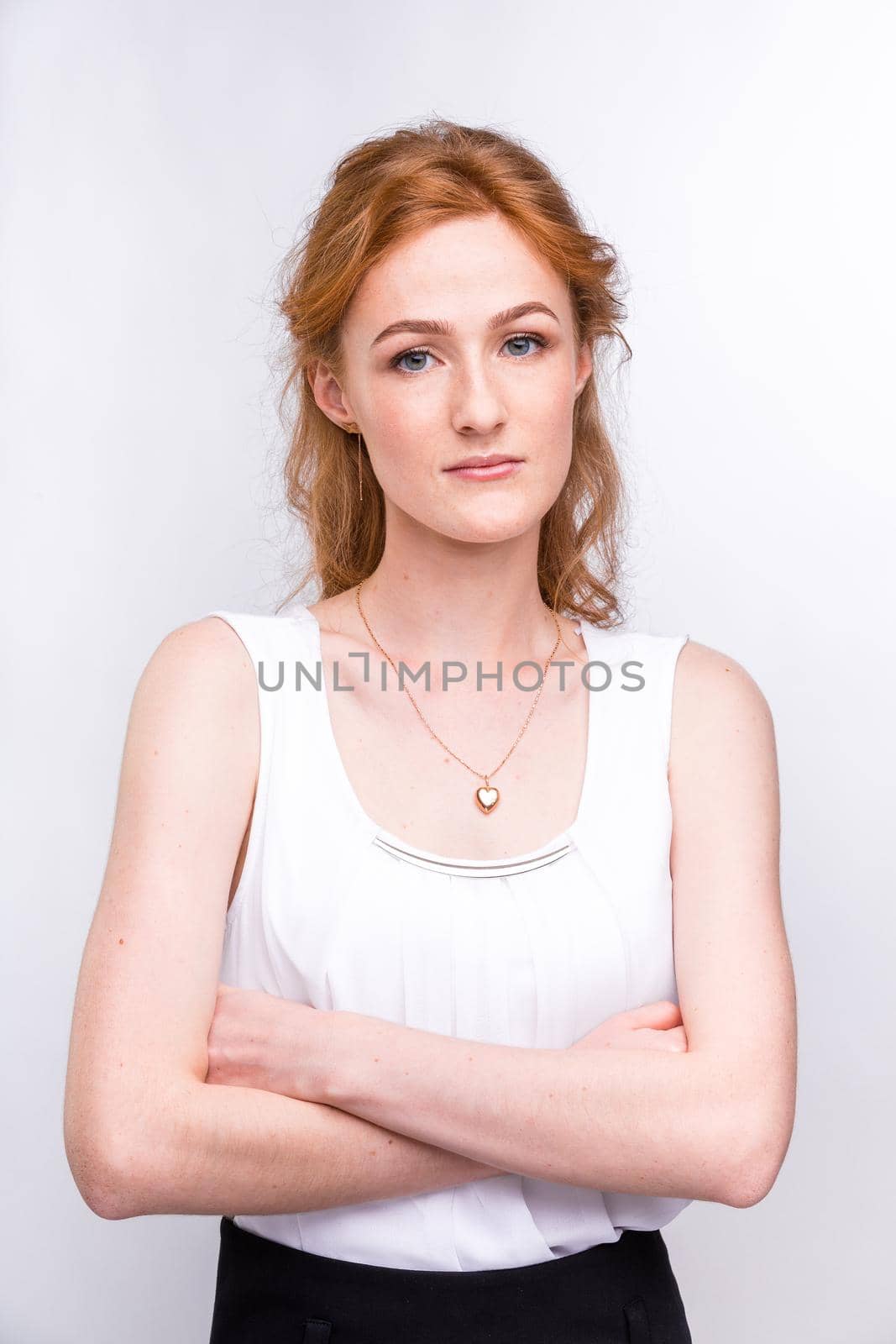 Portrait of a beautiful young woman of European, Caucasian nationality with long red hair and freckles on her face posing on a white background in the studio. Close-up student girl in a white blouse by Tomashevska