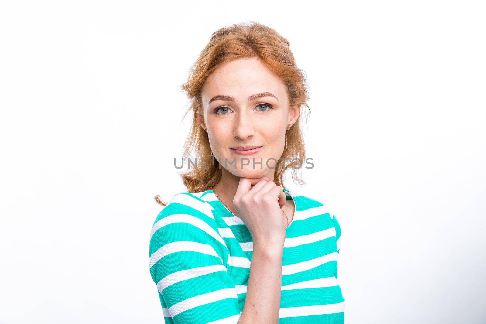 Close-up portrait of a young, beautiful woman with red curly hair in a summer dress with strips of blue in the studio on a gray background. Theme of summer vacation, tourism and summer clothes.