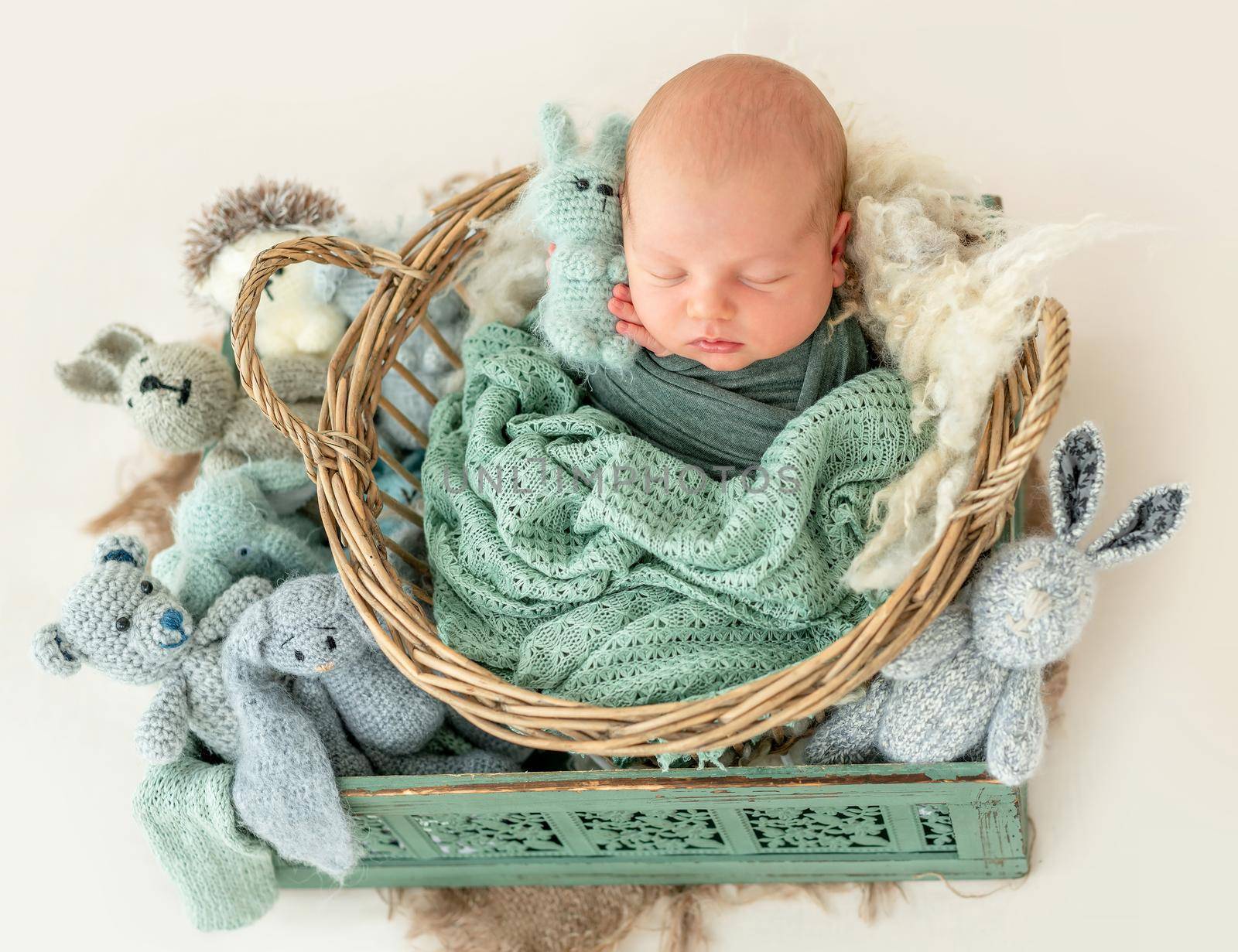 Cute newborn boy wrapped in a blanket sleep inside the basket with the toys