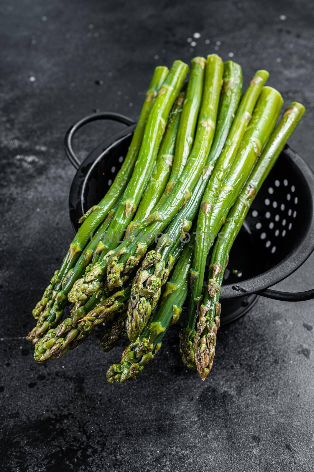 Raw green asparagus in a old colander. Black background. Top view by Composter