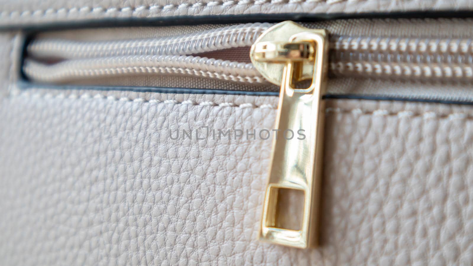 Natural or artificial leather texture. Fragment of a beige or powdery bag with a zipper and stitching. Zipper or clasp bag design element. Bovine skin texture with snake. Macro photo, selective focus