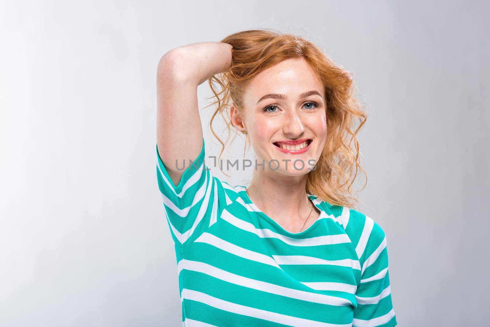 Close-up portrait of a young, beautiful woman with red curly hair in a summer dress with strips of blue in the studio on a gray background. Theme of summer vacation, tourism and summer clothes.