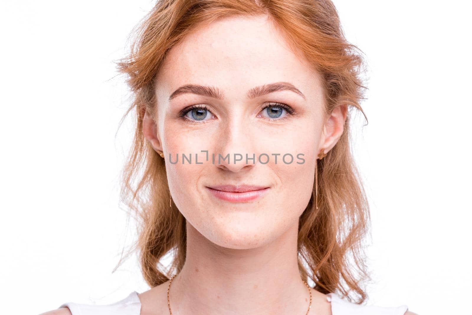 Portrait of a beautiful young woman of European, Caucasian nationality with long red hair and freckles on her face posing on a white background in the studio. Close-up student girl in a white blouse.