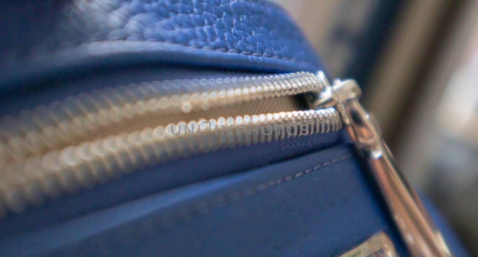 Natural or artificial leather texture. Fragment of a blue bag with a zipper and stitching. Zipper or clasp bag design element. Bovine skin texture with snake. Macro photo, selective focus