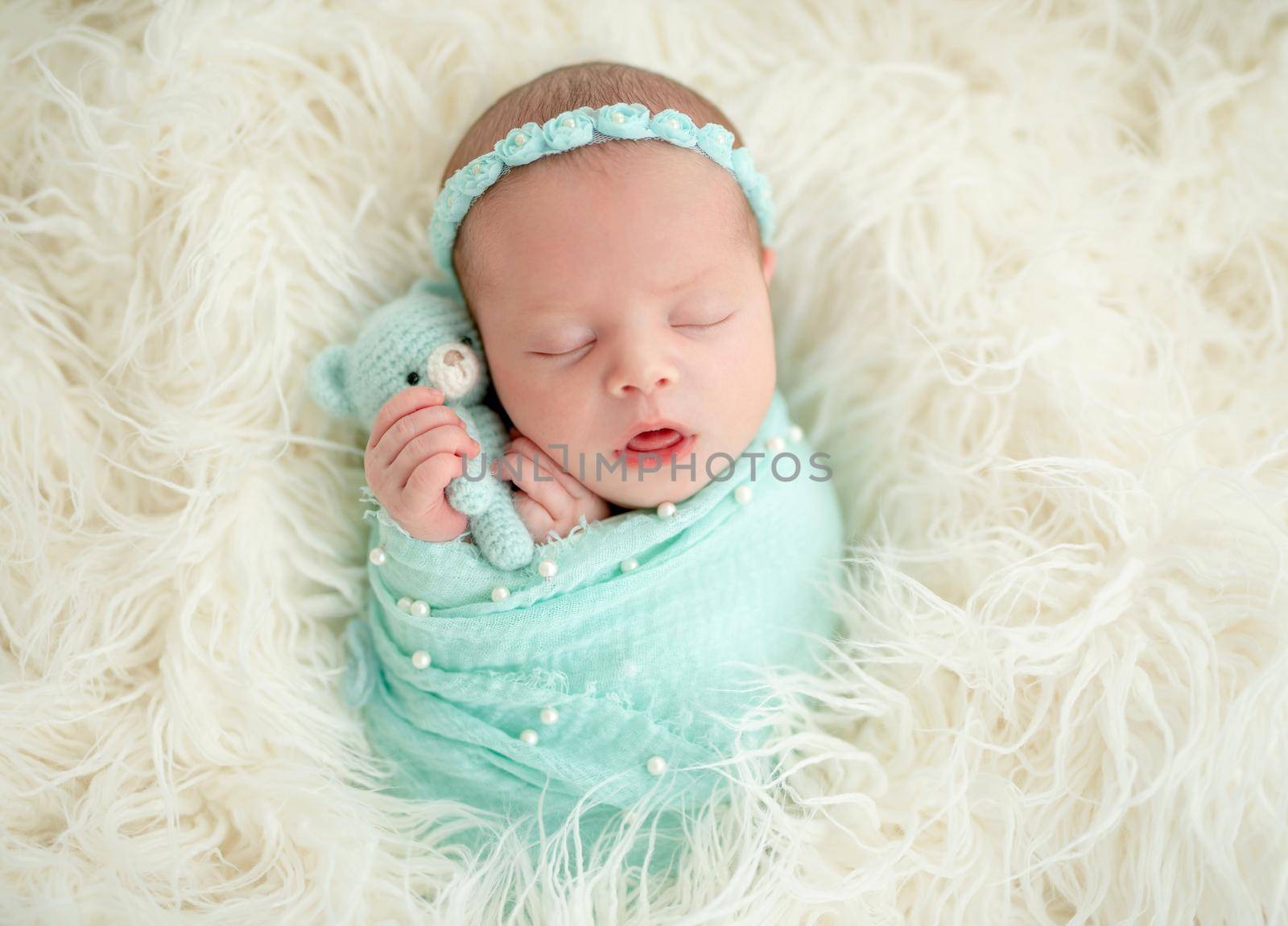 Sleeping adorable newborn baby child, in blue colored blanket and with floral headband