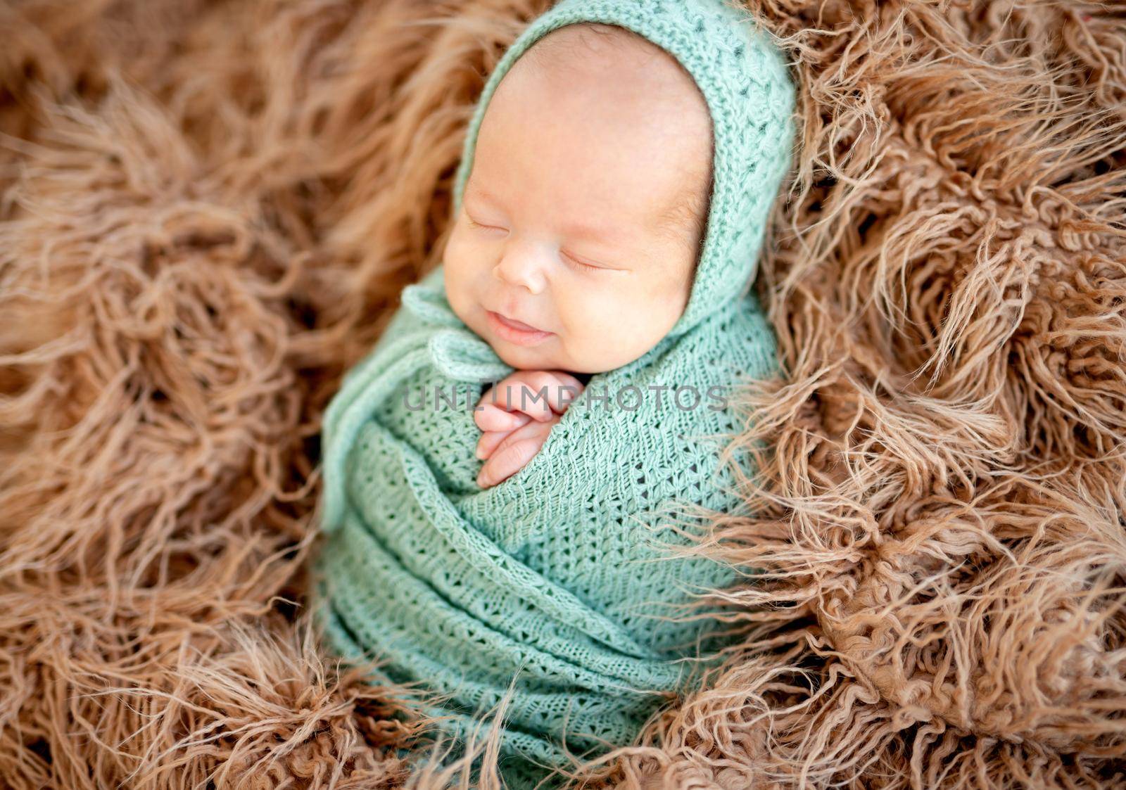 Smiling asleep newborn covered with knitted blanket