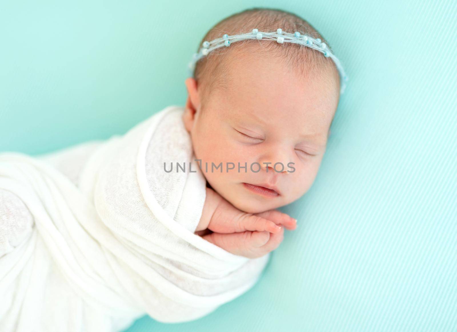 Sleeping adorable newborn baby child, in blue colored blanket and with floral headband