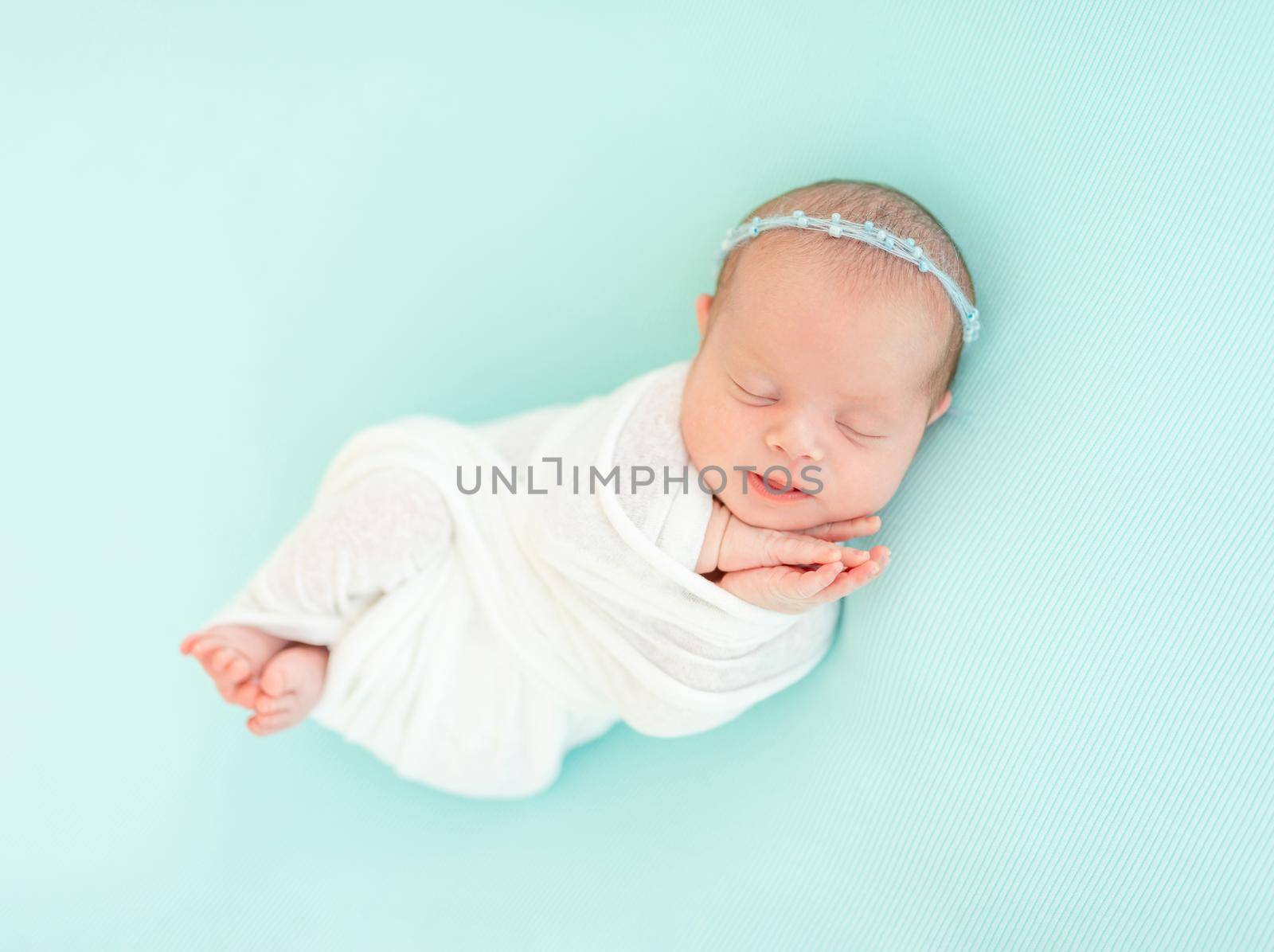 Sleeping adorable newborn baby child, in blue colored blanket and with floral headband