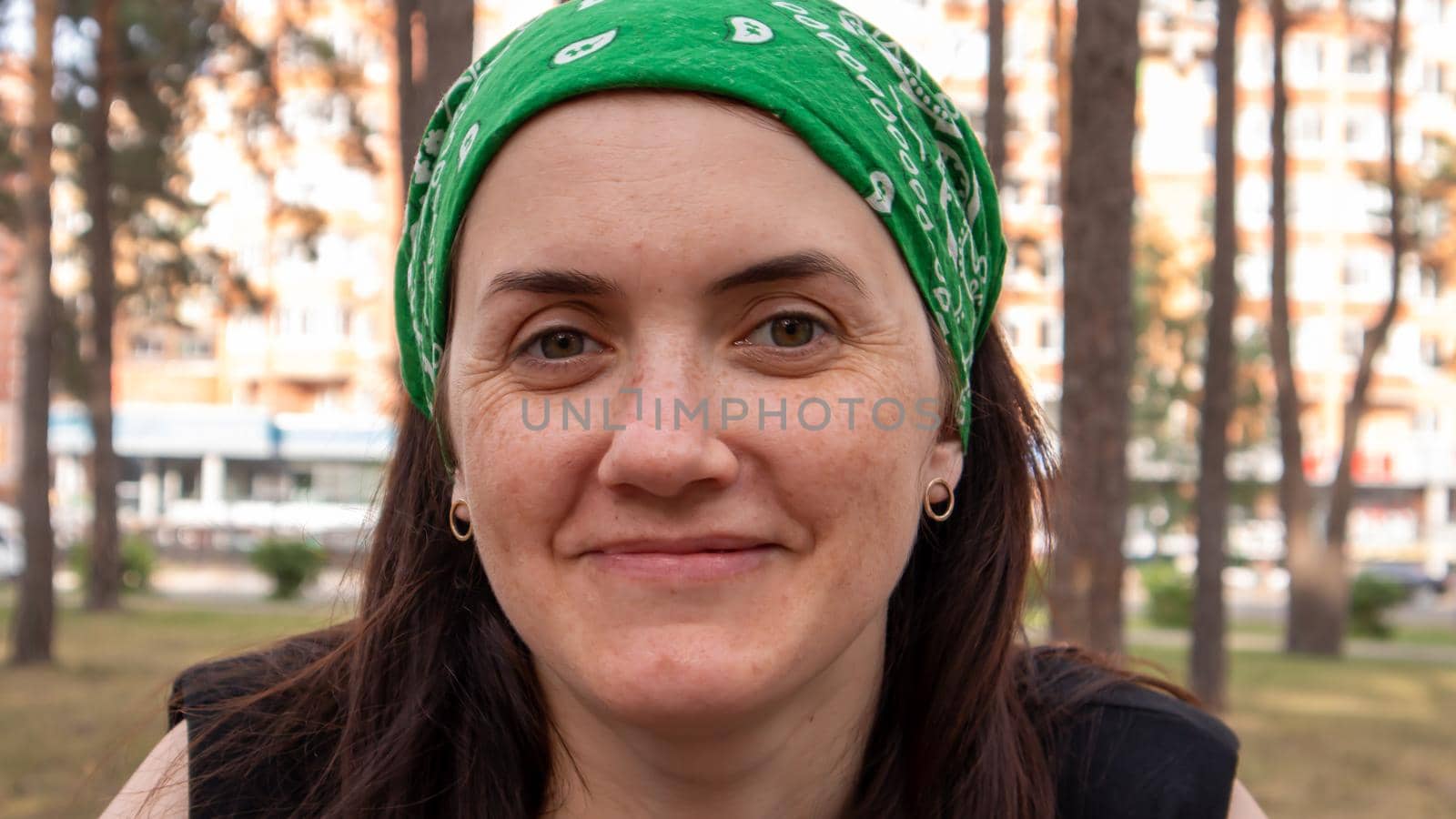 Close-up portrait. Beautiful young woman without makeup in a black T-shirt and a green headdress from the sun on a sunny summer day outdoors. Sunlight