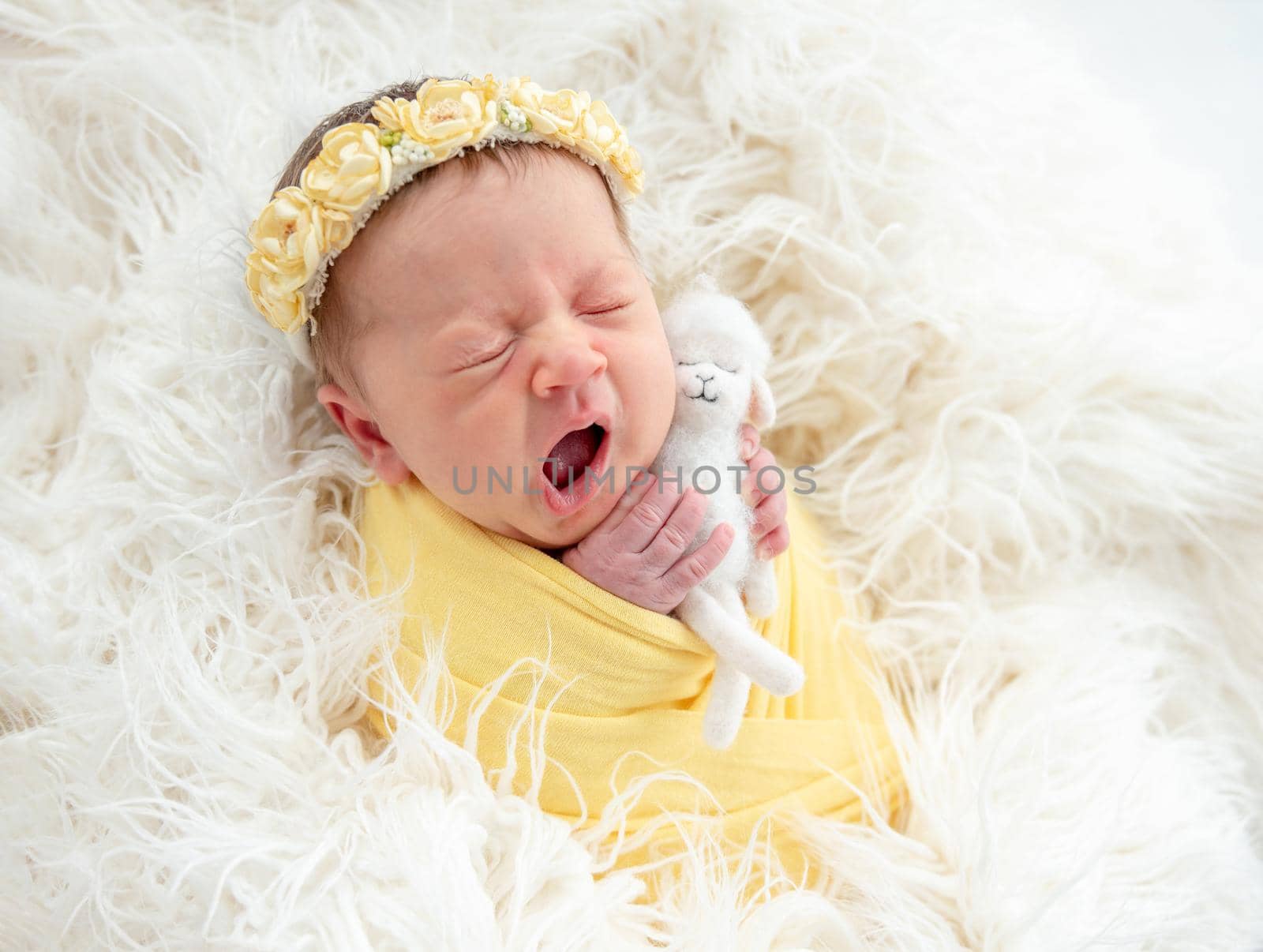 Yawning newborn girl in diadem holding toy